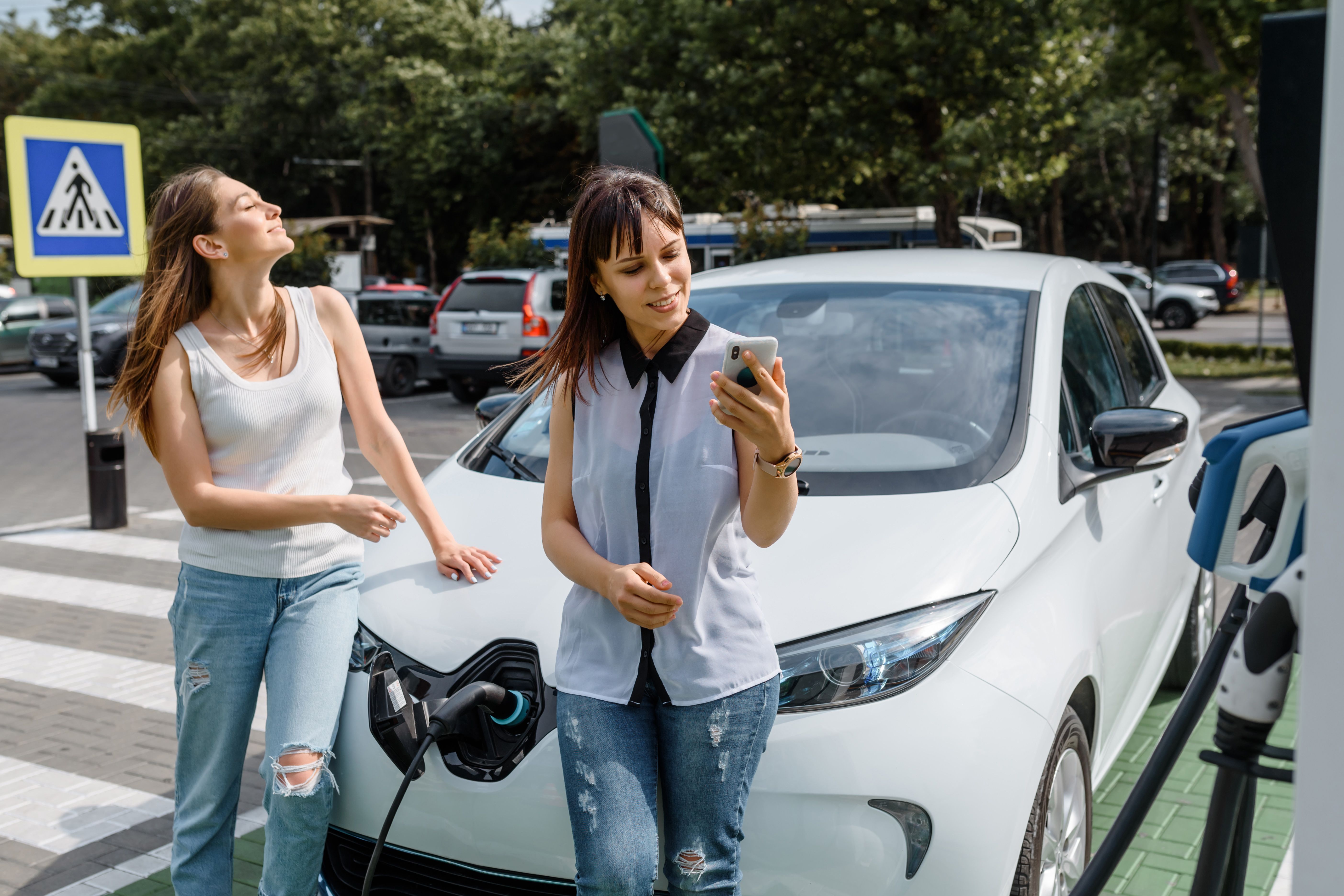 Deux femmes rechargent leur véhicule électrique sur une aire d'autoroute