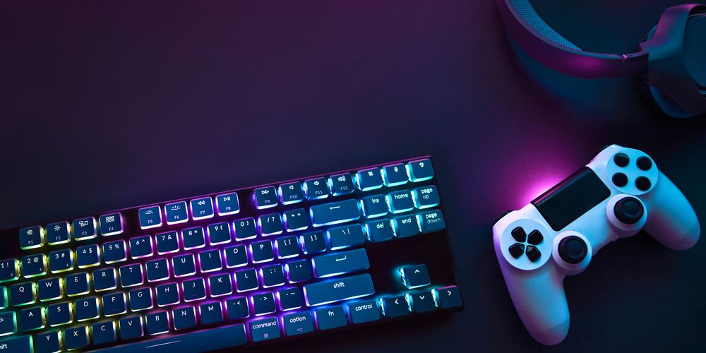 Gaming-tillbehör: tangentbord med färgglad bakgrundsbelysning, en trådlös handkontroll och ett par hörlurar.