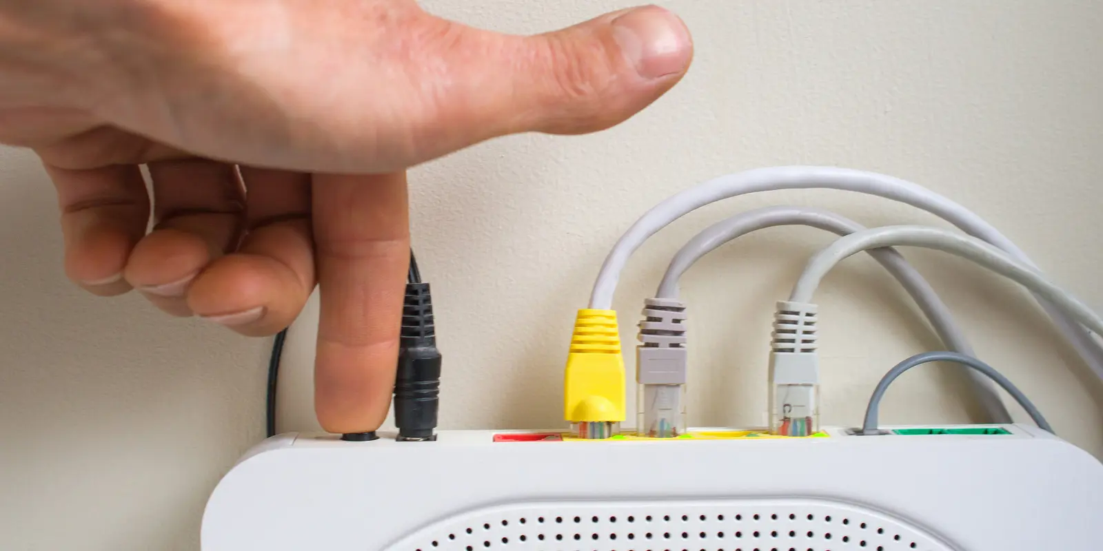 Nærbilde av oversiden av en en hånd som trykker inn reset-knappen på en router.