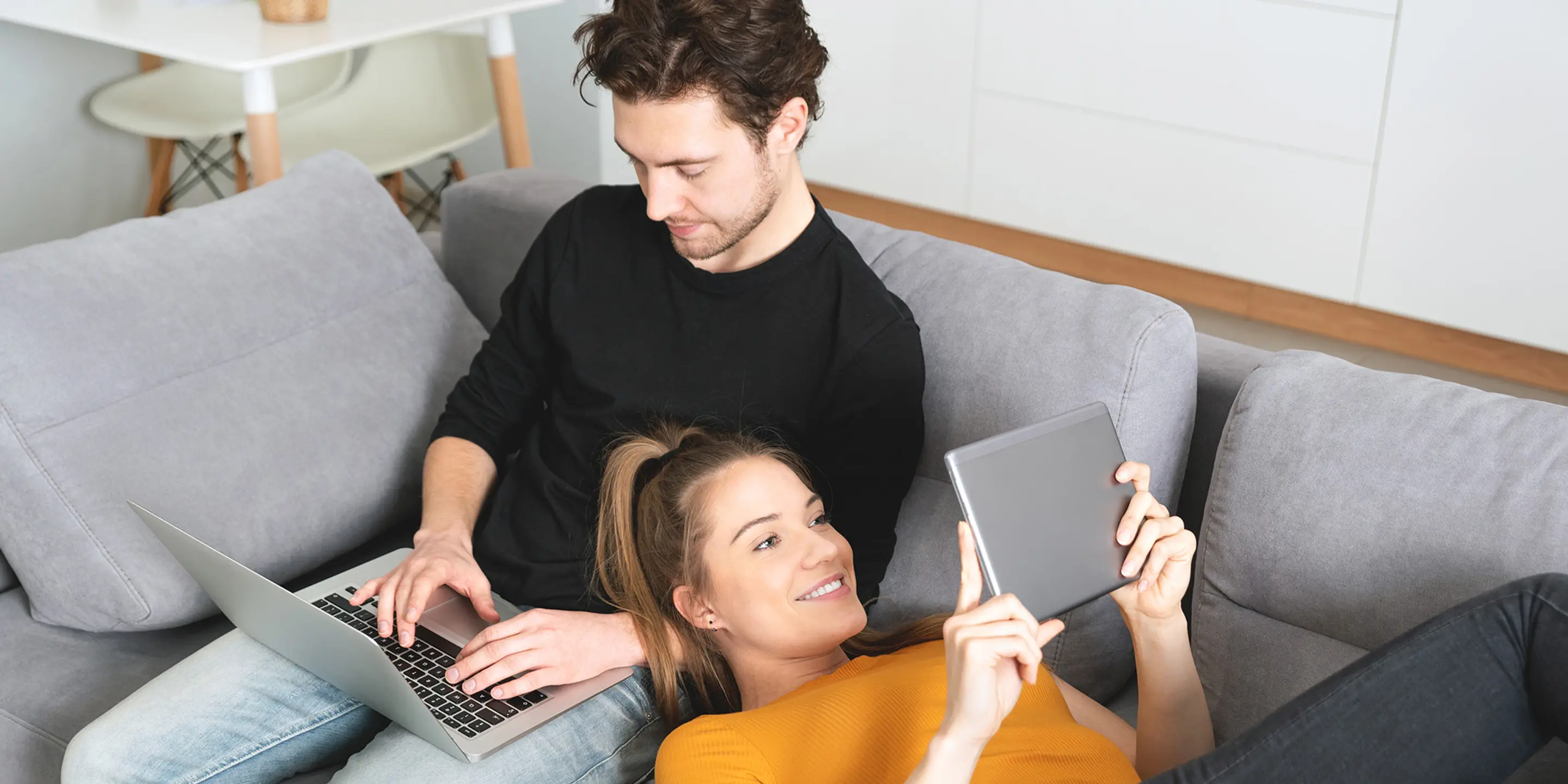 Bilde av et ungt par som sitter i en sofa på hver sin skjerm.