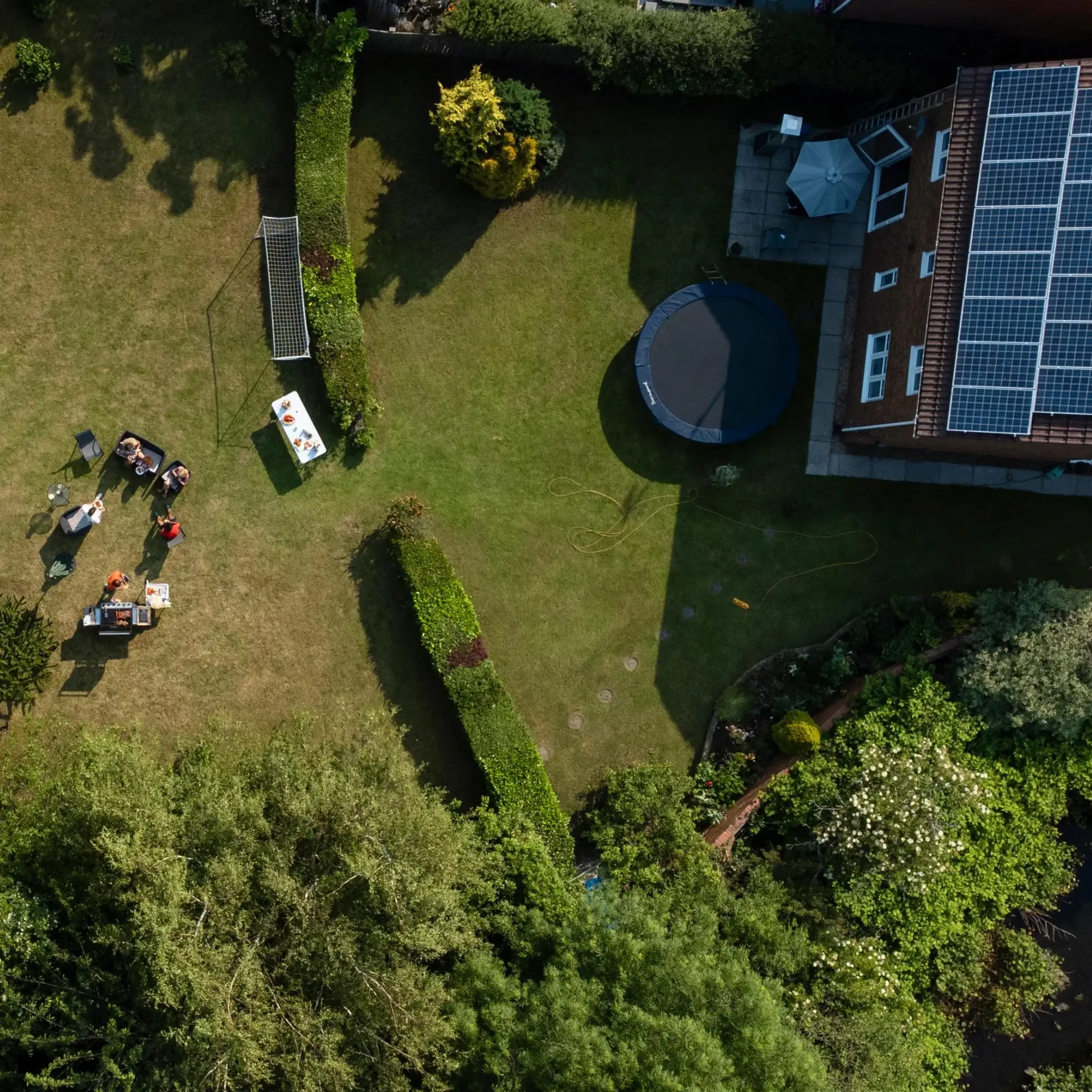 Flygfoto ovanifrån på tomt med en familj som umgås utomhus invid en villa med solceller på taket.