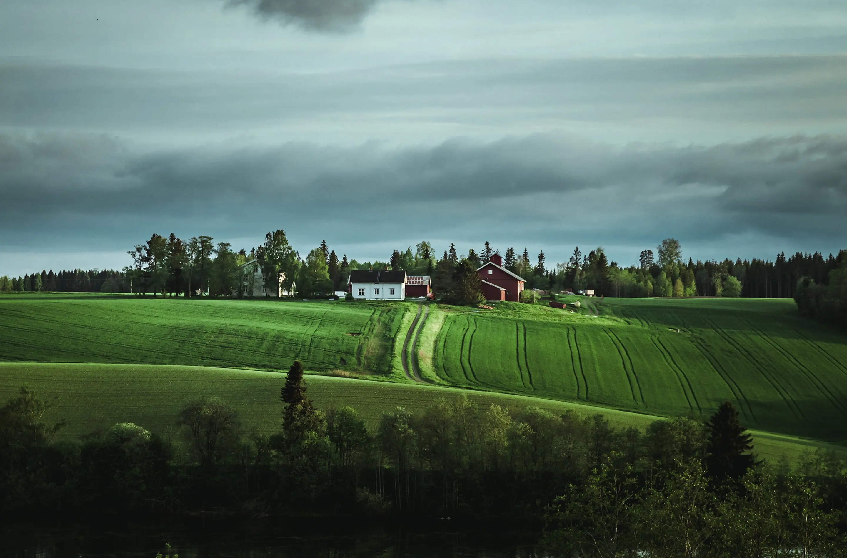 Bilde av et grønt jorde og en gård midt i bildet.