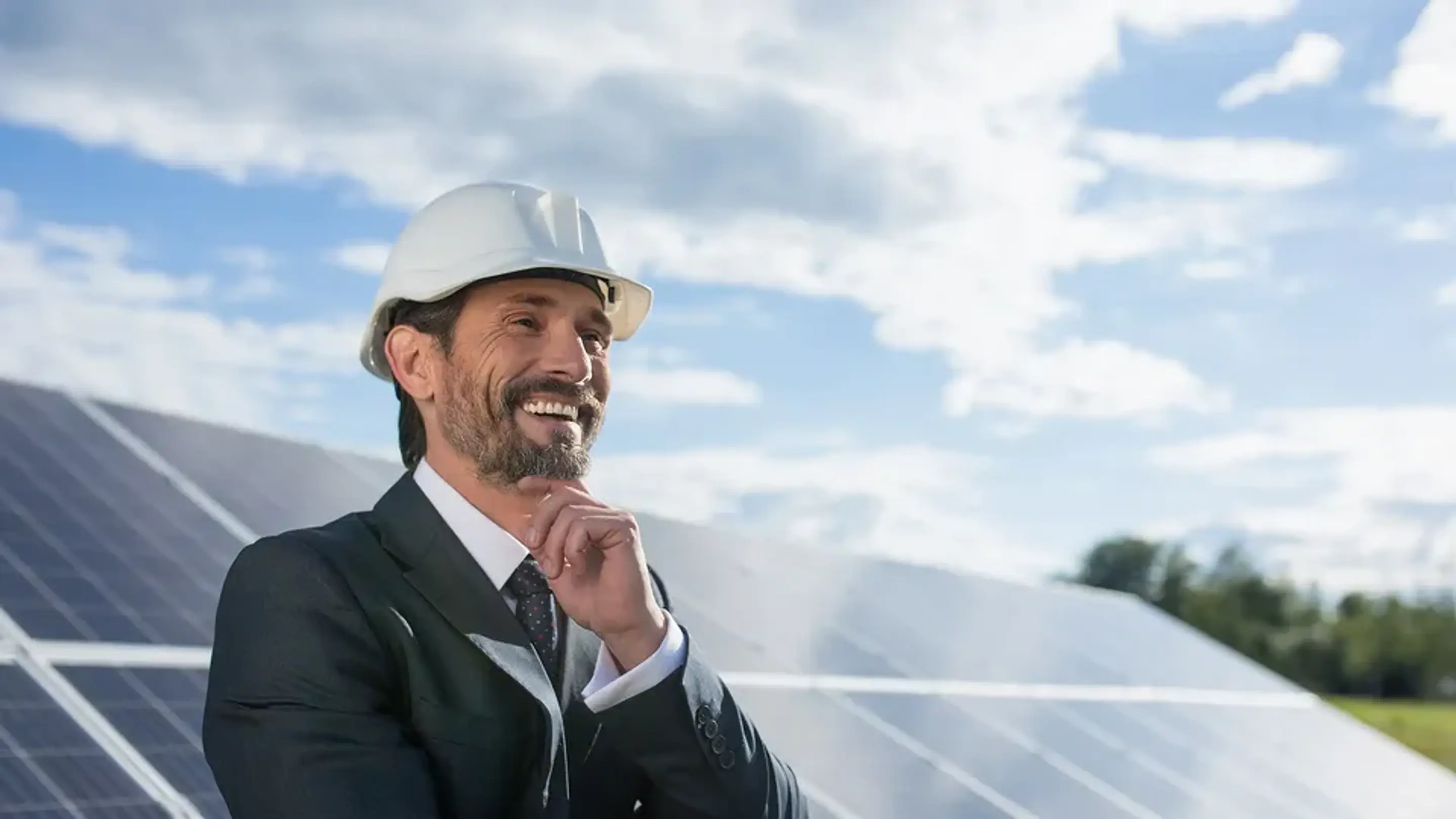 En leende man med skyddshjälm står framför en rad med solpaneler.