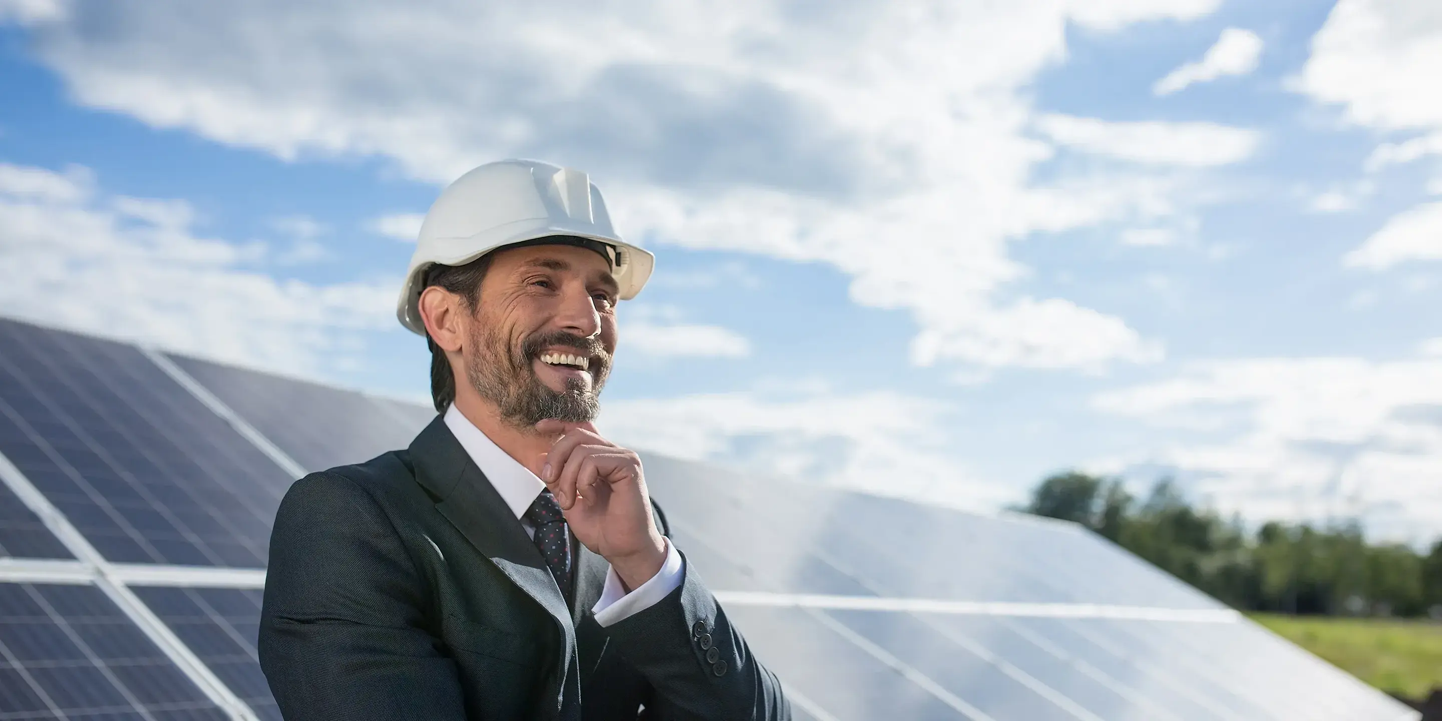 En leende man med skyddshjälm står framför en rad med solpaneler.