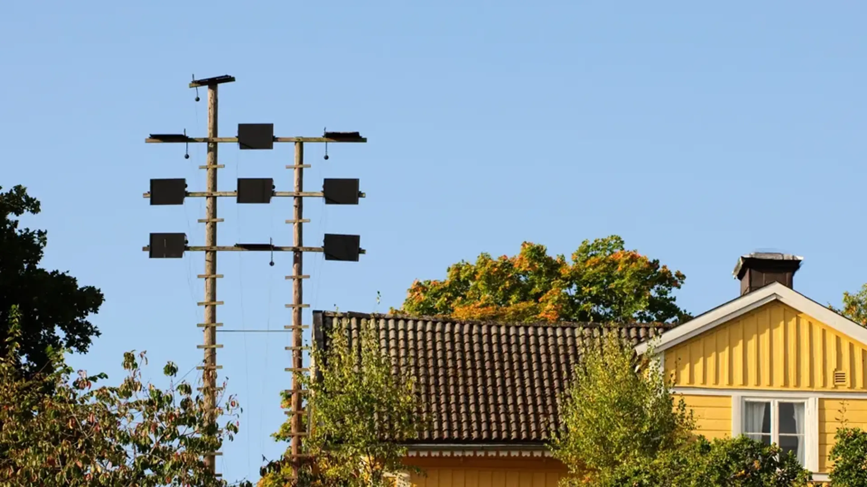 Gult trähus med elstolpar och ledningar i ett villaområde.