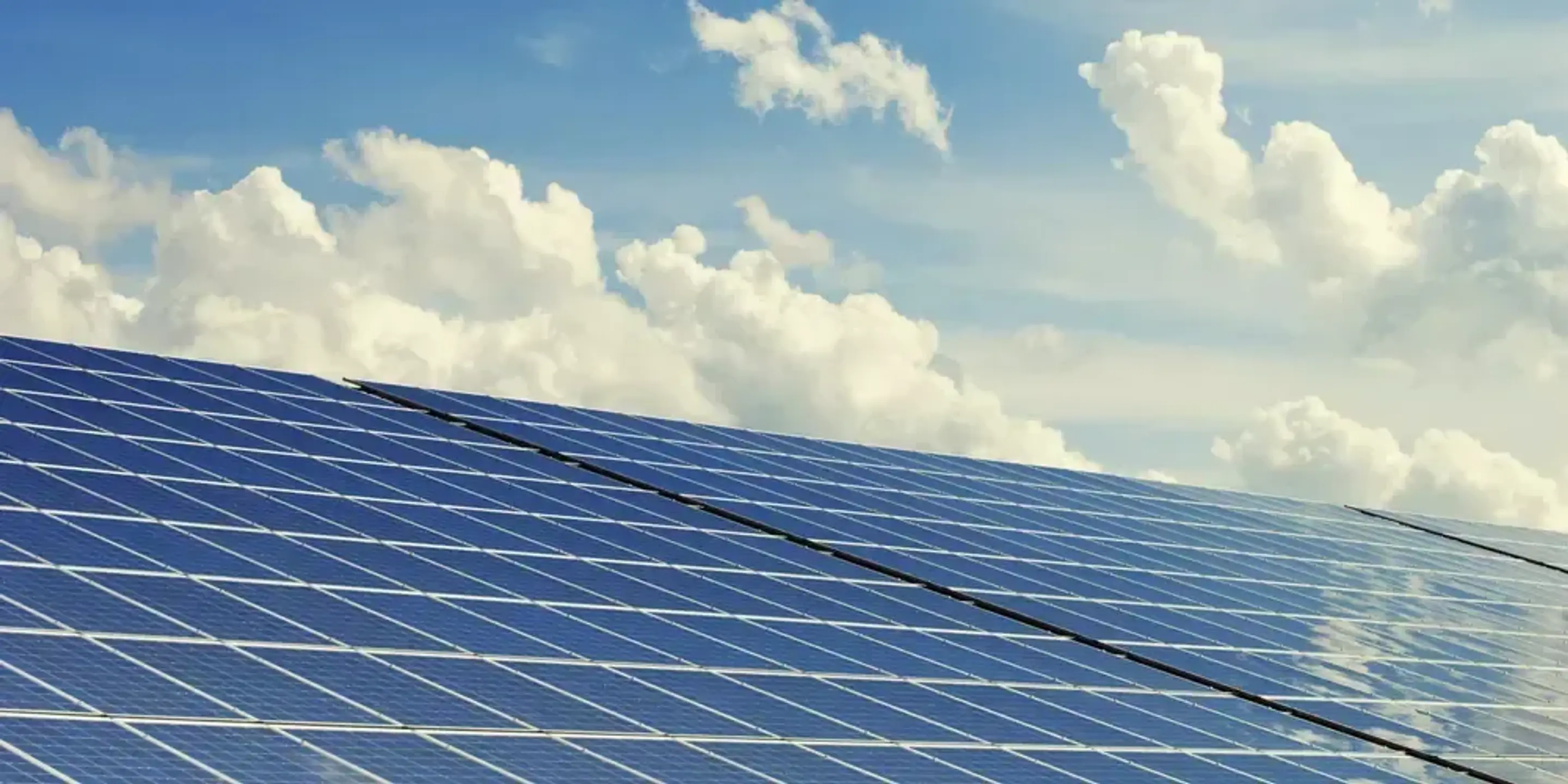 Solceller på ett tak framför en himmel med vita moln.