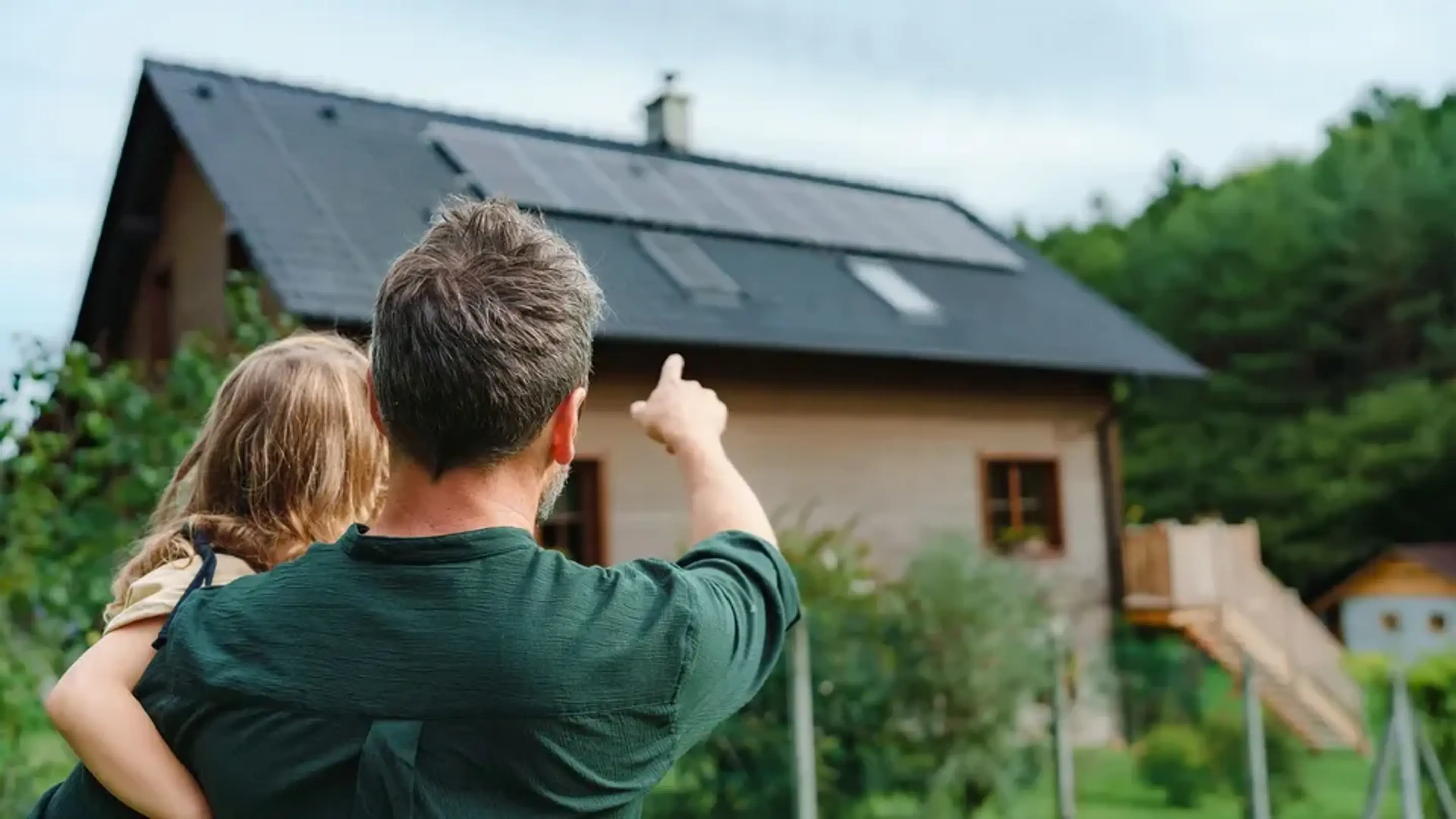Far med barn på armen peger på solceller på taget