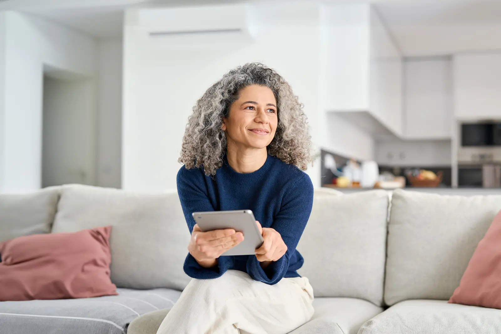 Kvinne som sitter i en sofa med en tablet og ser til høyre.