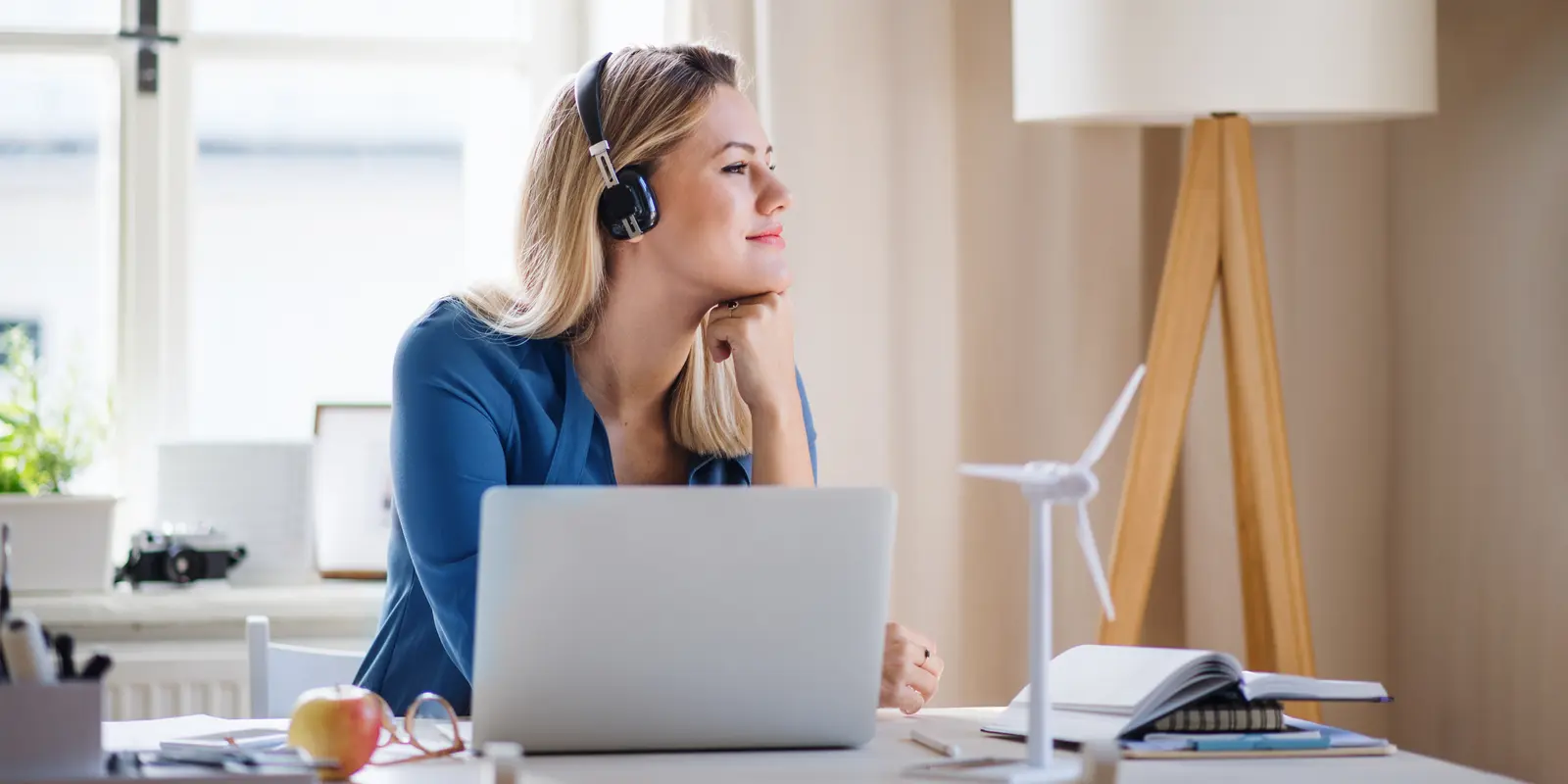 Bilde av en kvinne som sitter på en pult foran en laptop og ser til høyre.