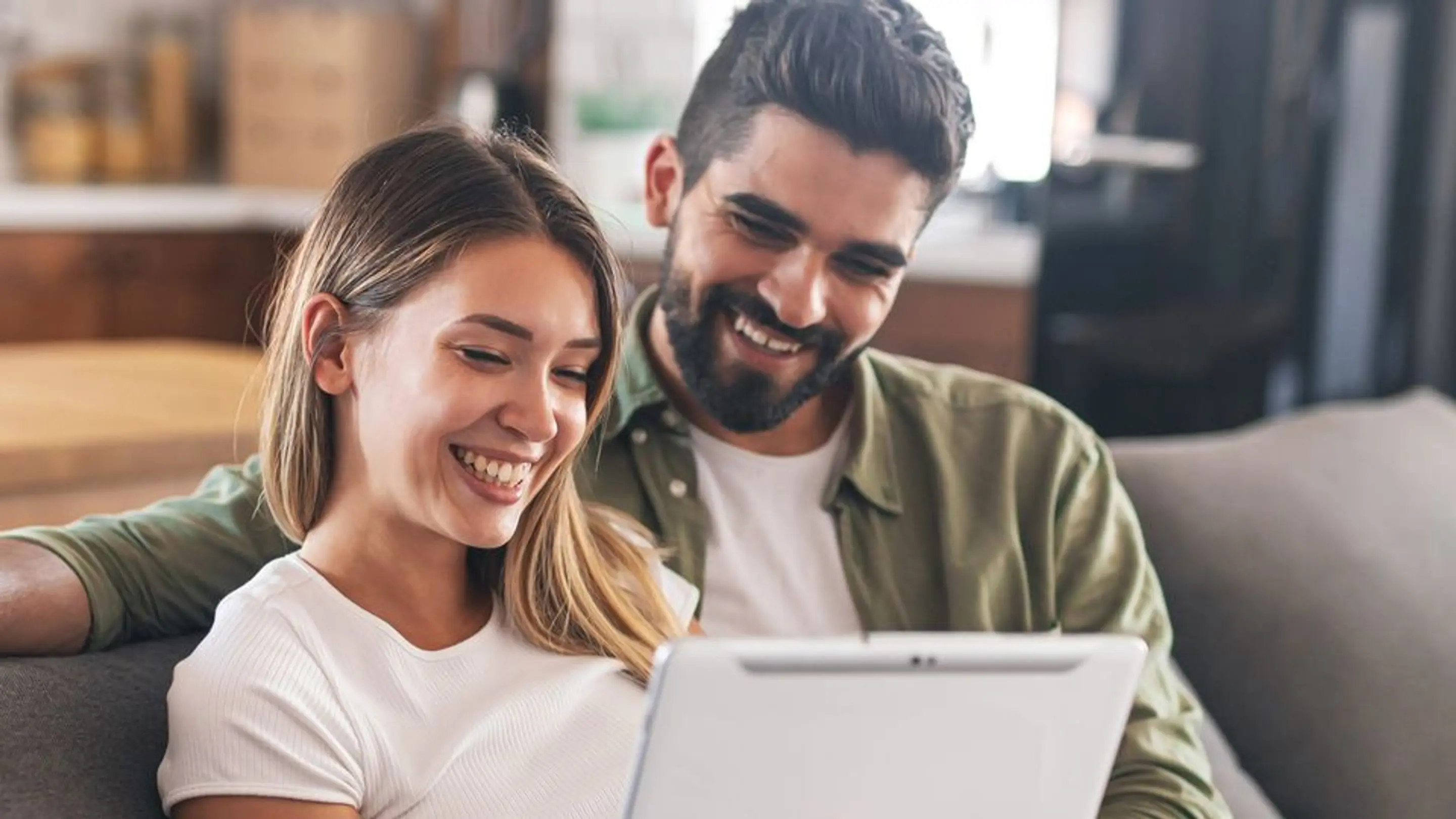 Bilde av et smilende par som ser på en skjerm mens de sitter i en sofa.