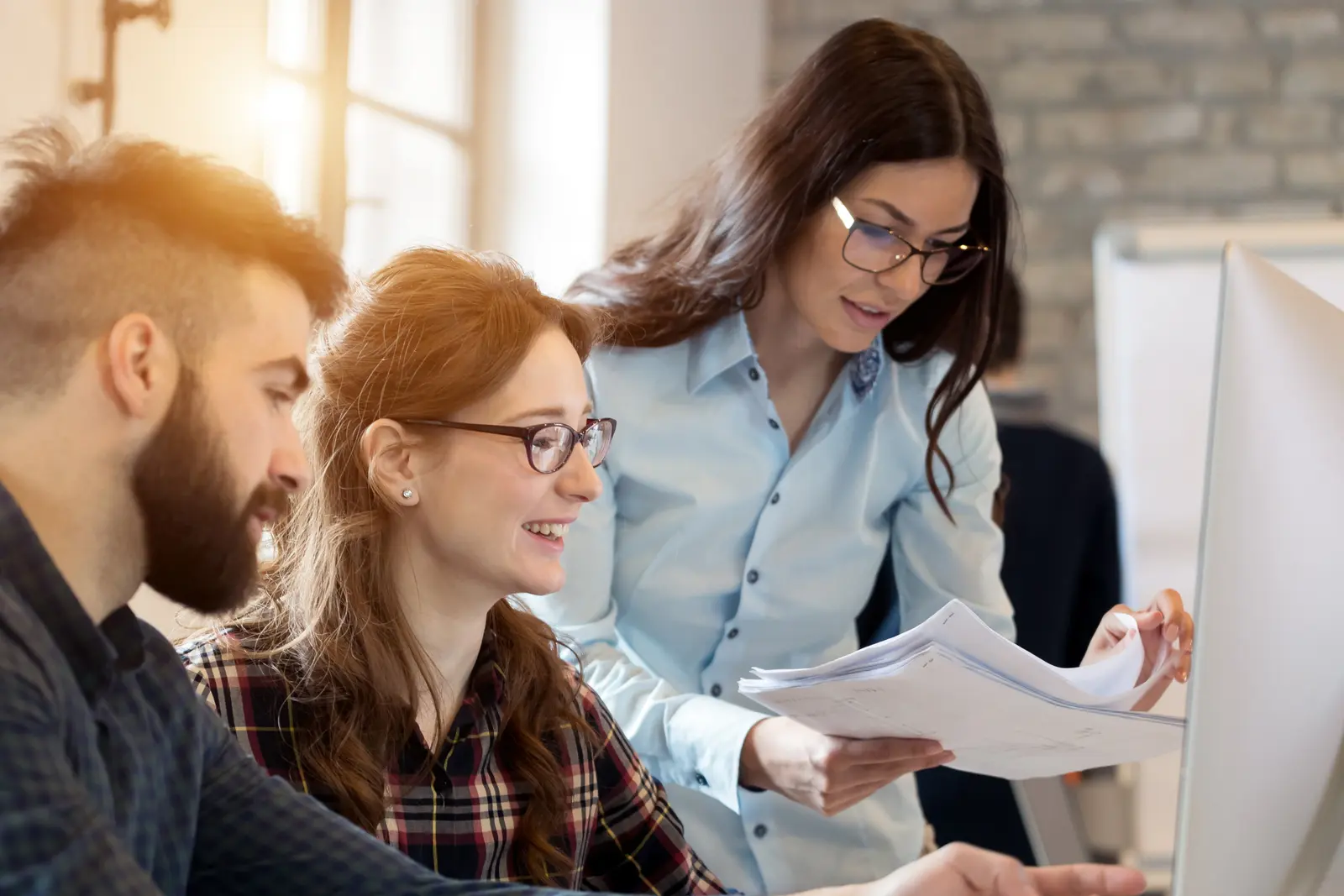 Bilde av tre ansatte som smiler og jobber sammen rundt en laptop.