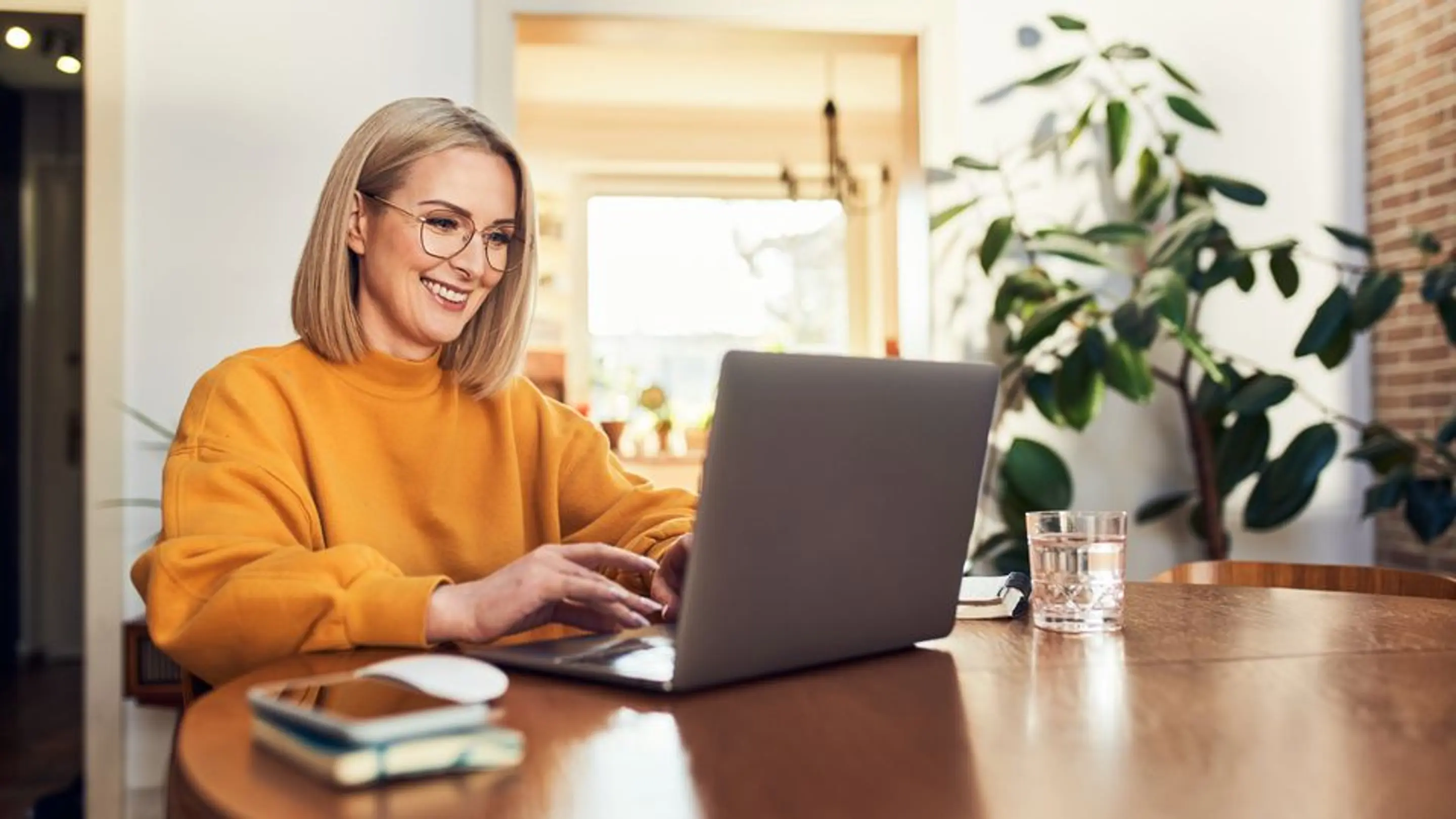 Bilde av en kvinner som smiler mens hun bruker en laptop til å fylle ut skjemaet på Bredbånd.no.