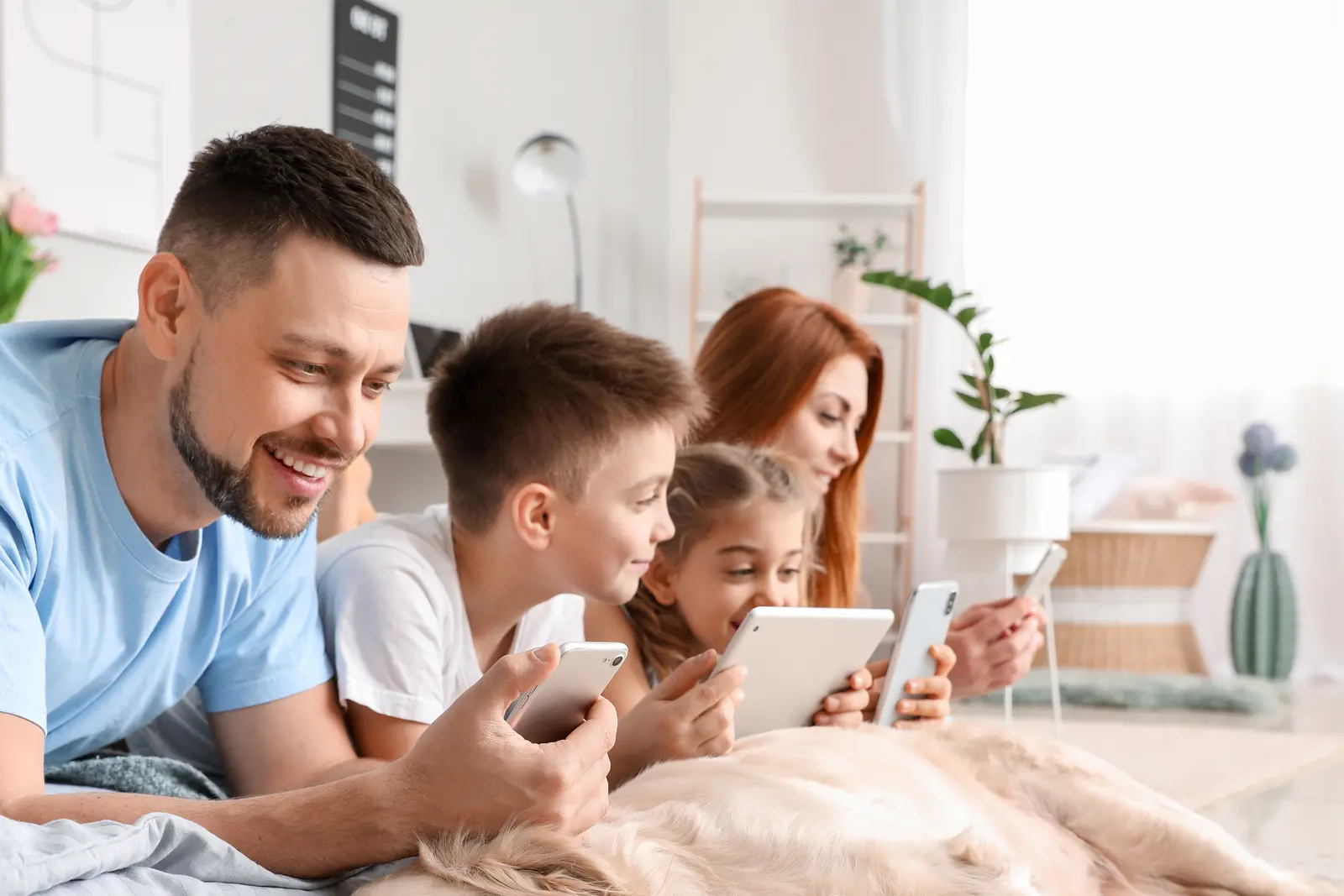 Bilde av en smilende familie som ligger på gulvet og ser på hver sin skjerm.
