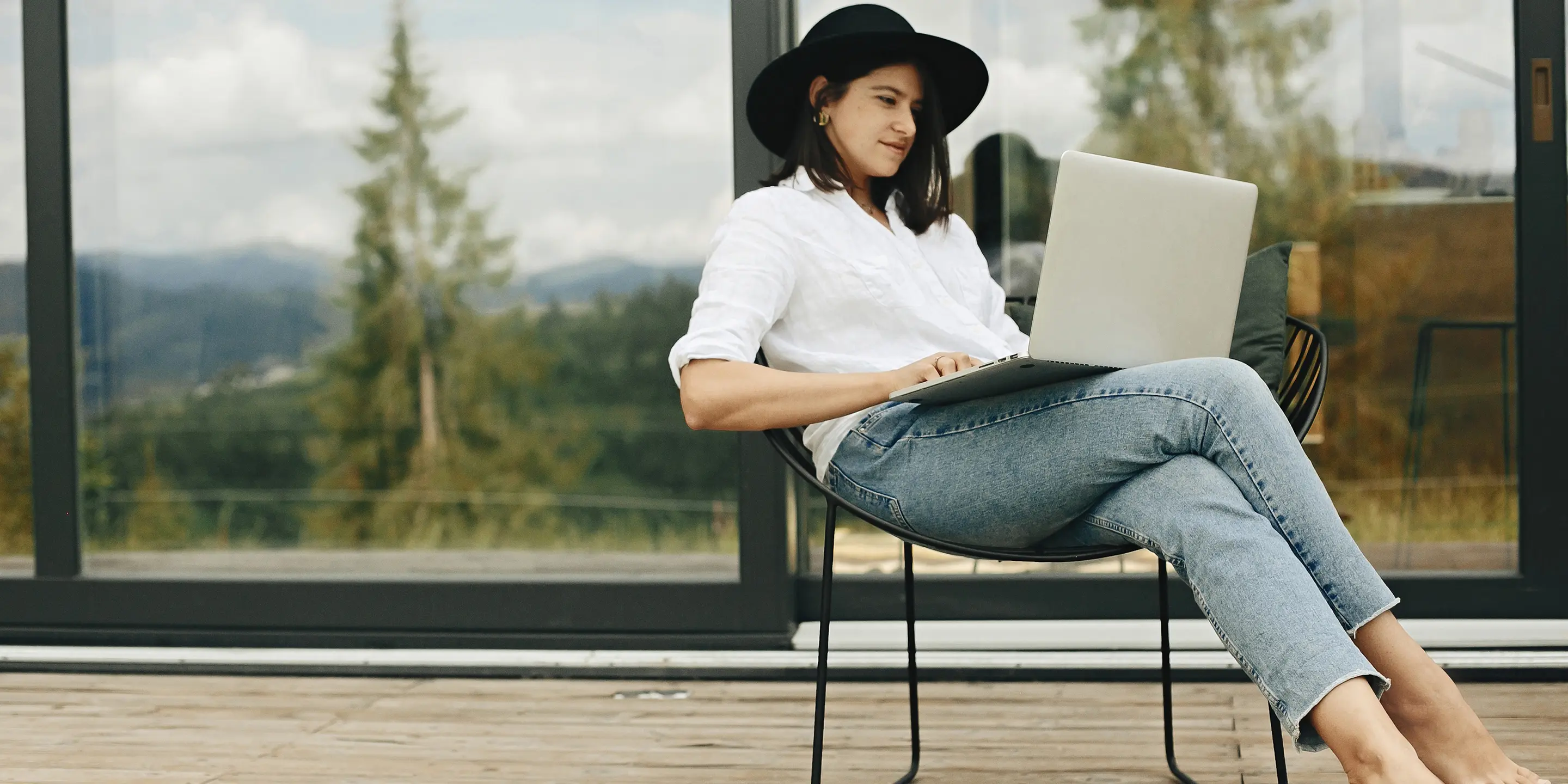 Bilde av en kvinne som sitter utenfor en hytte med en pc på fanget.
