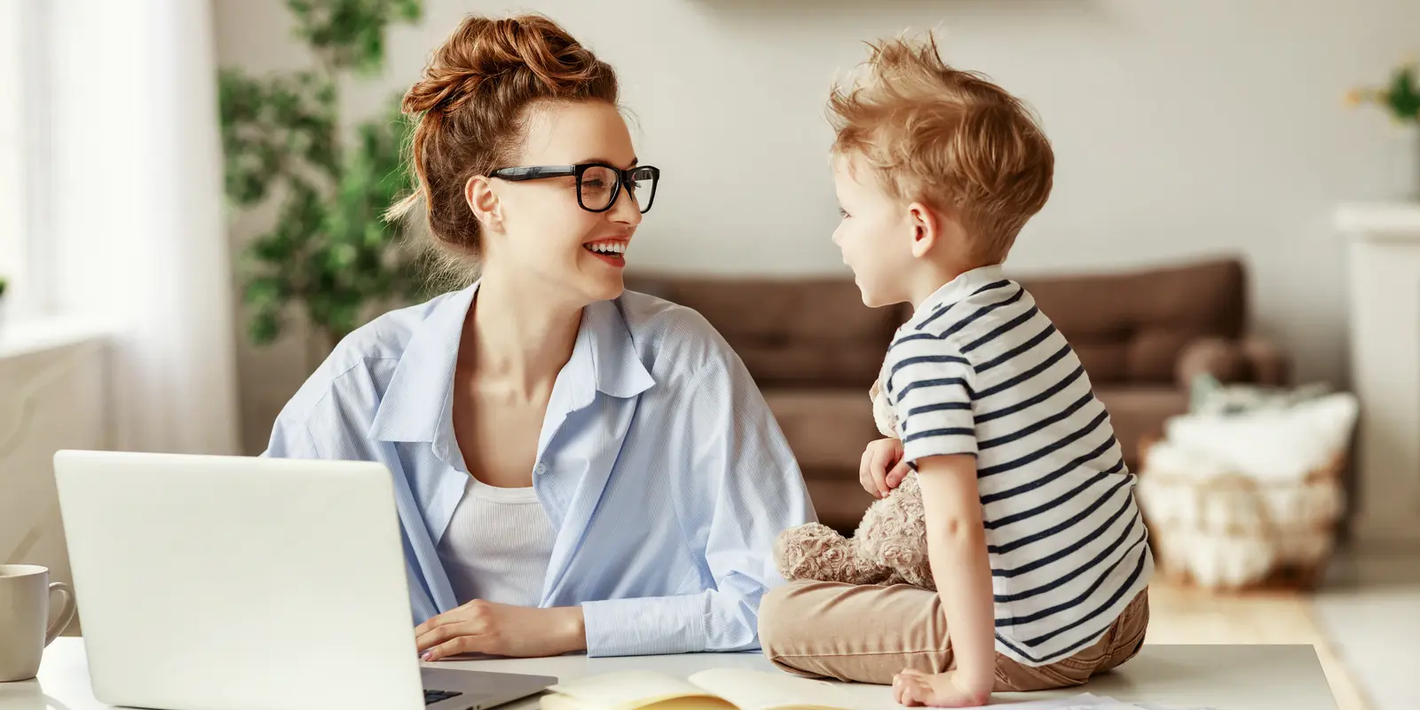 Bilde av en kvinne som smiler mot barnet sitt som sitter på bordet ved siden av en laptop.