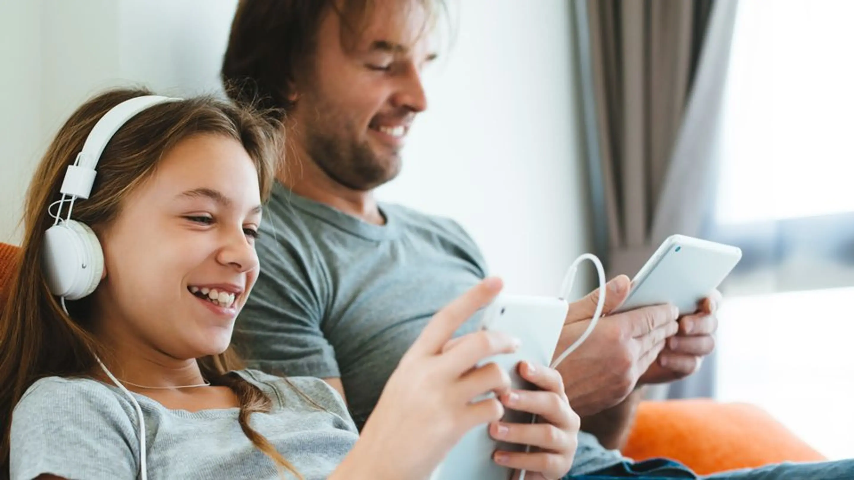 Bilde av en far og datter som sitter på hver sin mobiltelefonon og smiler ved siden av hverandre.