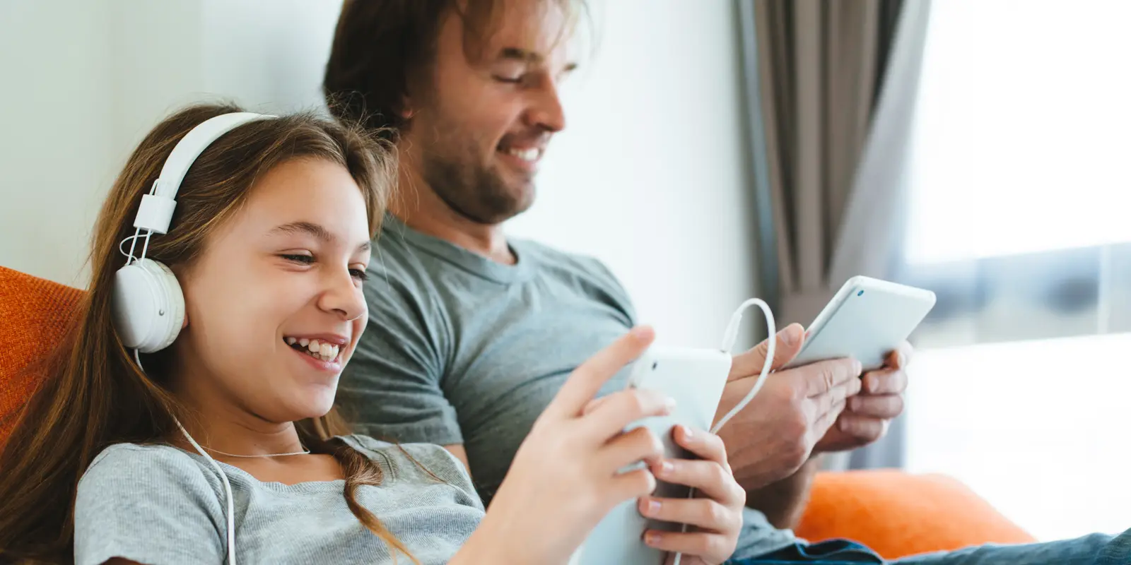 Bilde av en far og datter som sitter på hver sin mobiltelefonon og smiler ved siden av hverandre.