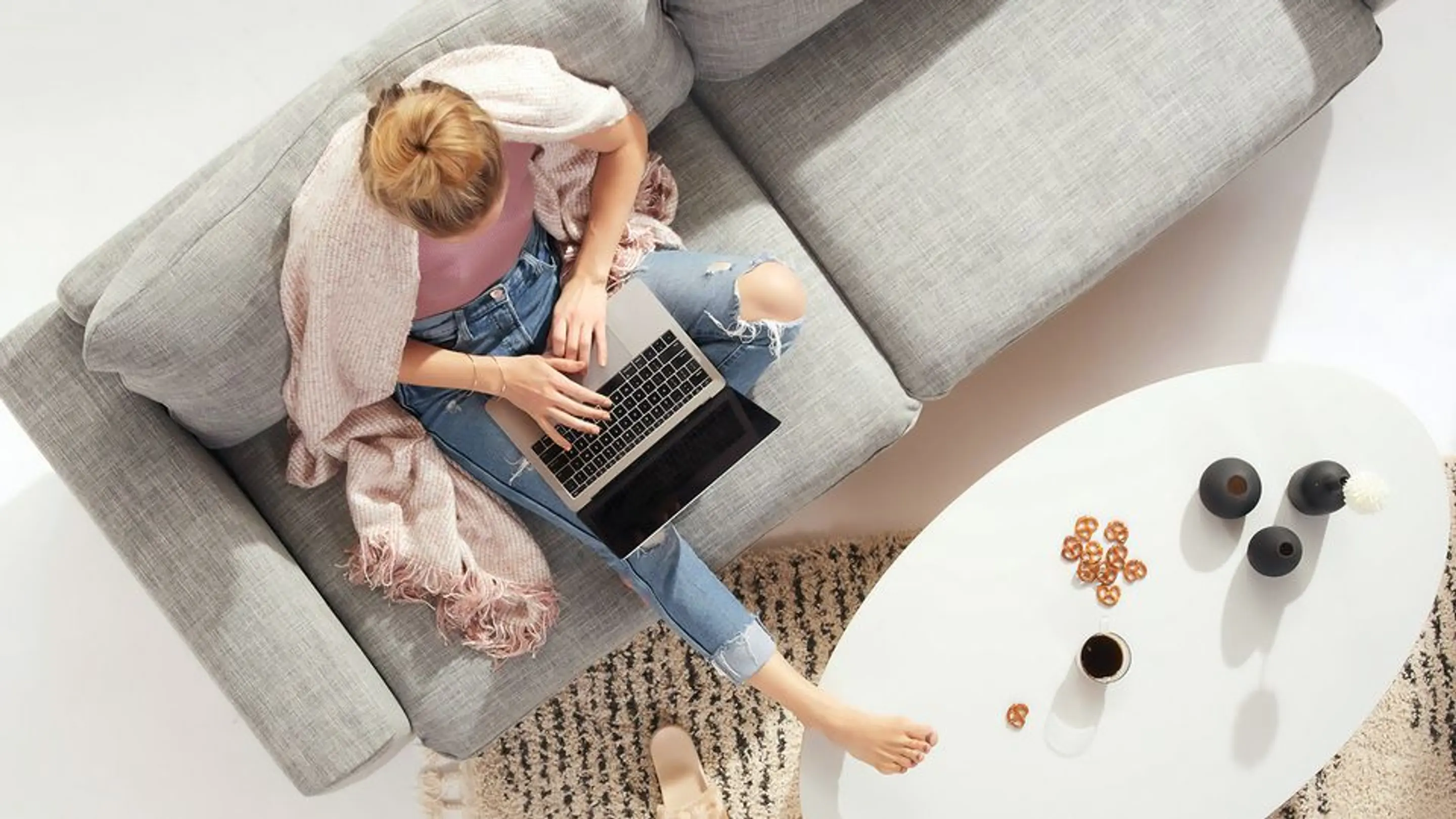 Bilde av en kvinne som skriver på en pc mens hun sitter i sofaen med et pledd over skuldrene.