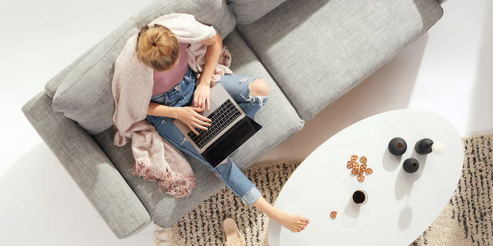 Bilde av en kvinne som skriver på en pc mens hun sitter i sofaen med et pledd over skuldrene.