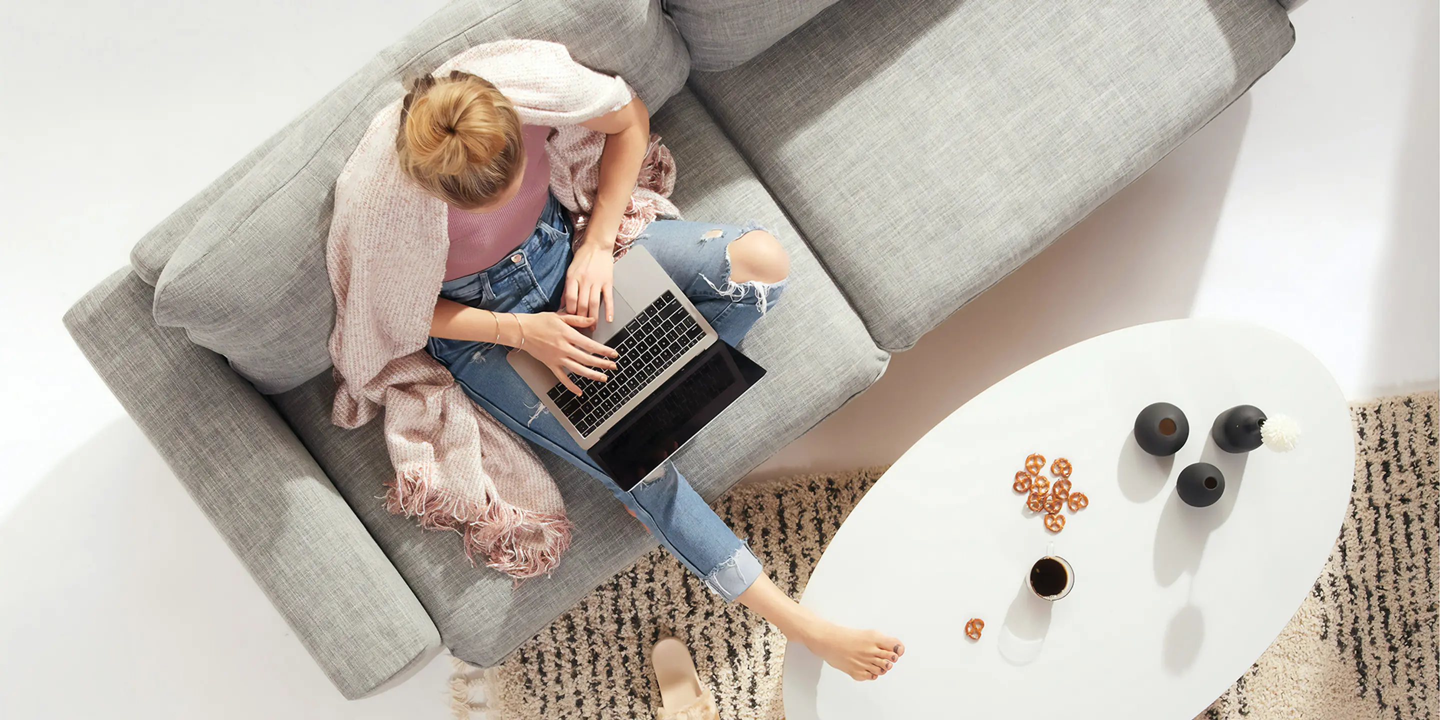 Bilde av en kvinne som skriver på en pc mens hun sitter i sofaen med et pledd over skuldrene.