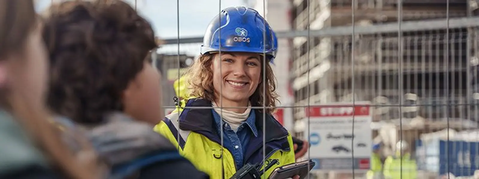 Bilde av en smilende dame med obos-merket vernehjelm inne på et anleggsområde.