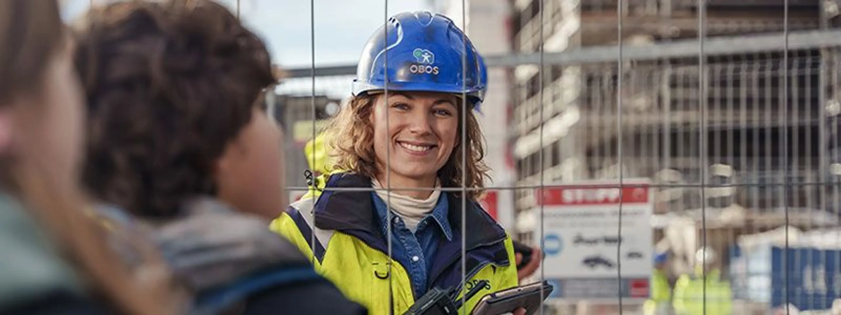 Bilde av en smilende dame med obos-merket vernehjelm inne på et anleggsområde.