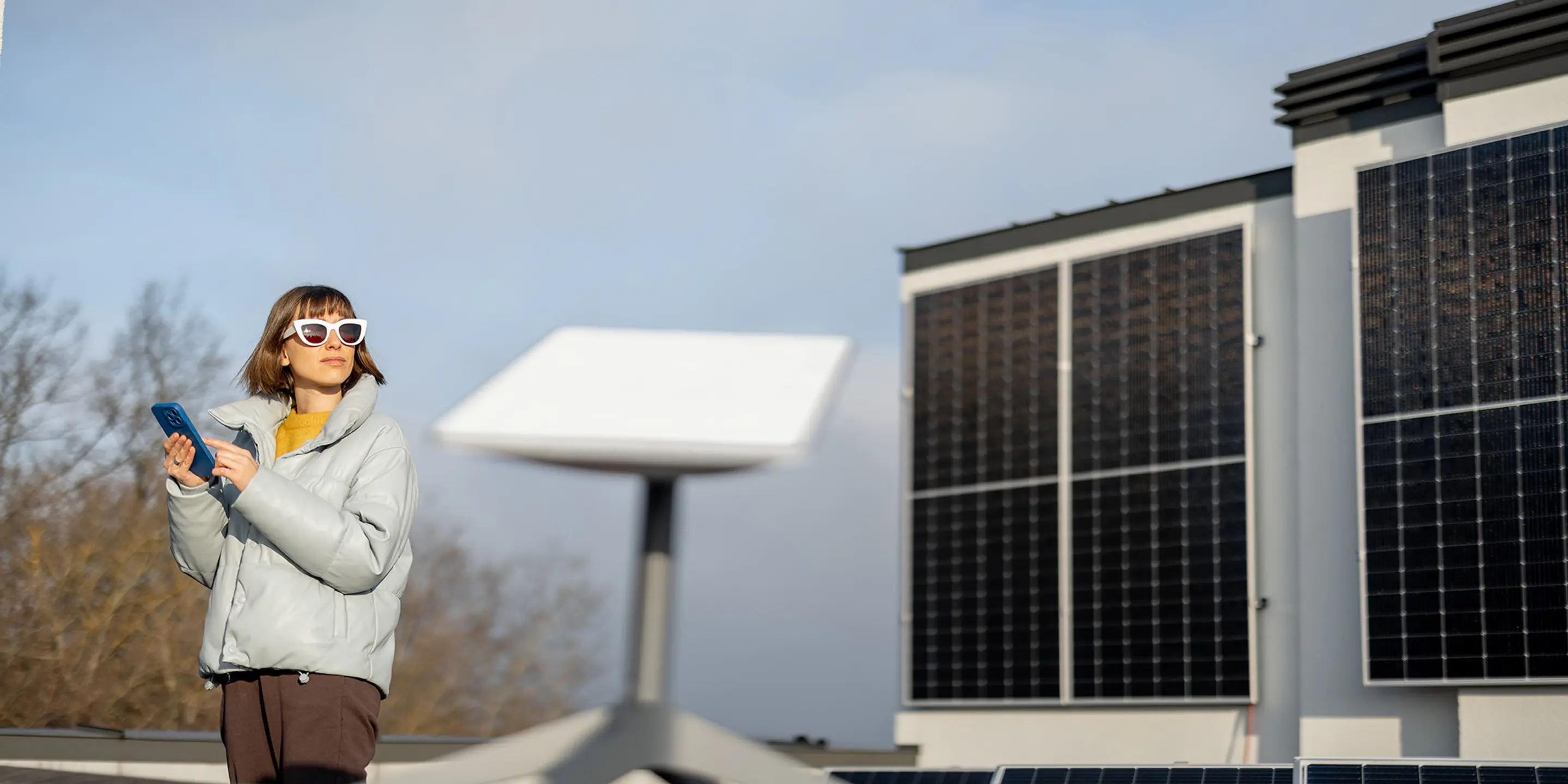 Bilde av en antenne til satellittbredbånd i forgrunnen med en kvinne som står i bakgrunnen og ser til siden.