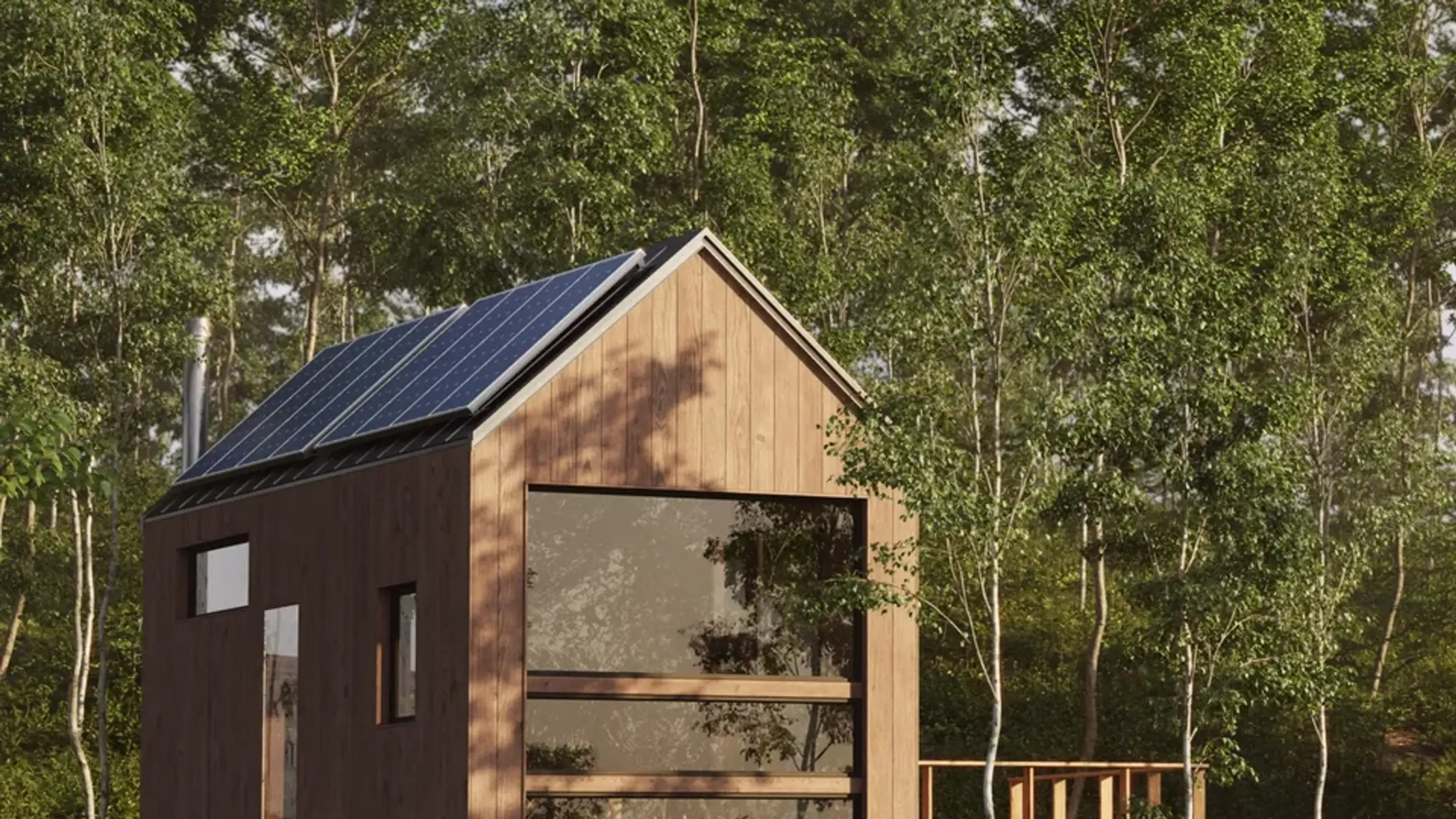 Ett litet trähus med sadeltak täckt av solpaneler, omgivet av tät grön skog, med stora fönster framtill och en enkel altan.