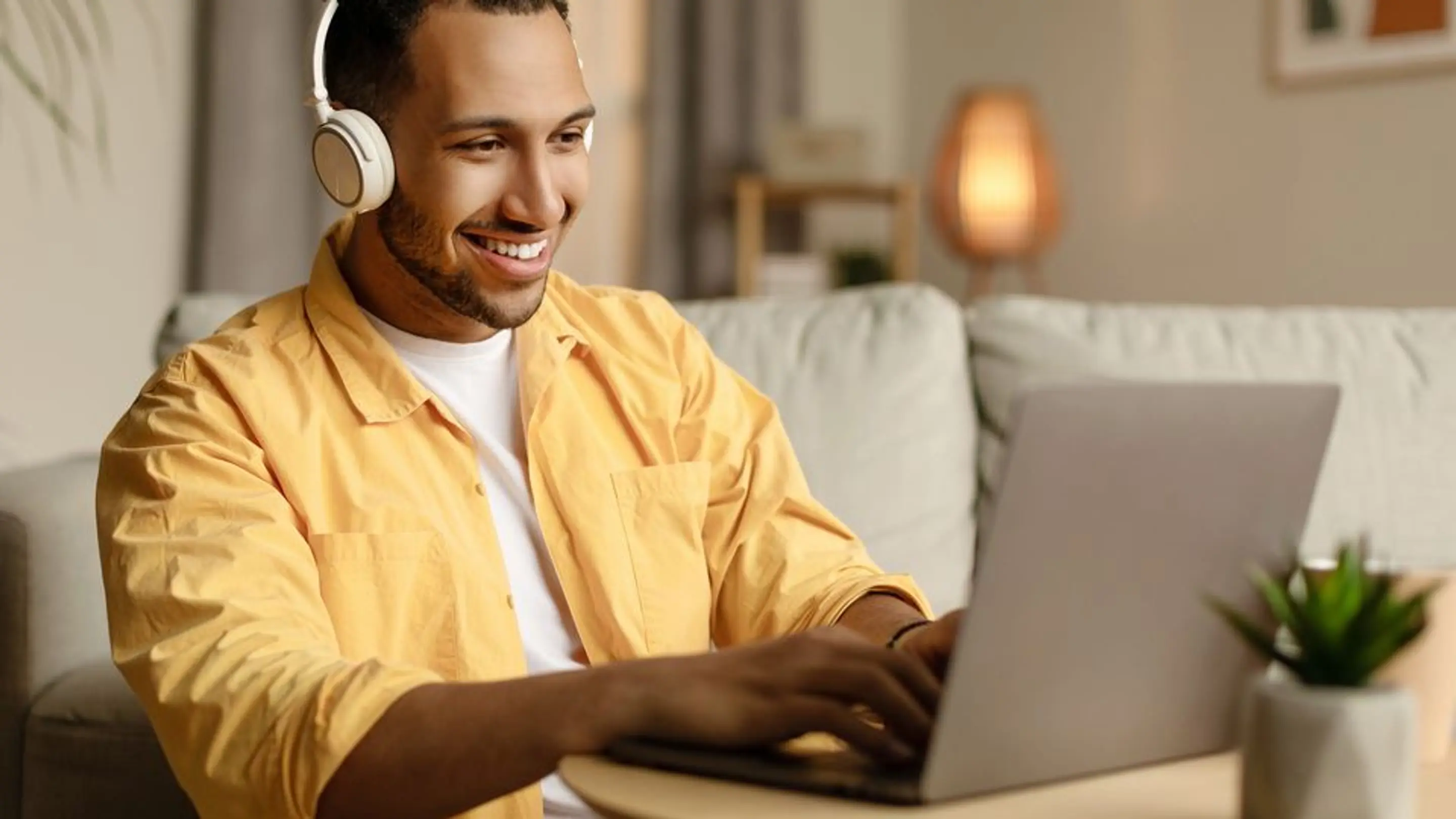 Bilde av en smilende mann med headset som sitter på en laptop.