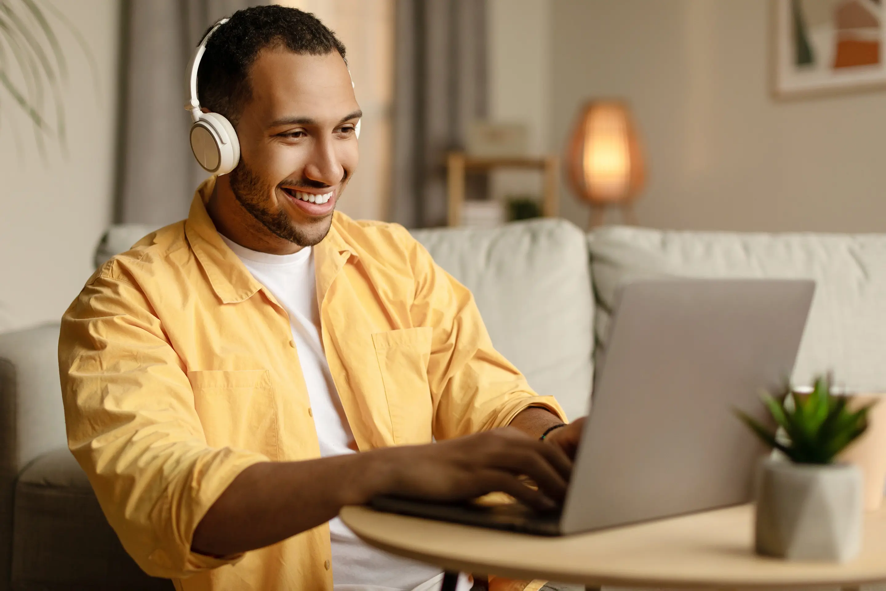 Bilde av en smilende mann med headset som sitter på en laptop.