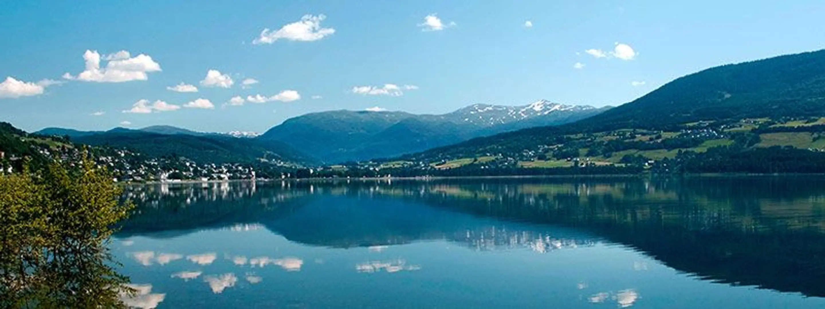Et solfylt landskapsbilde utover et vann med fjell i bakgrunnen