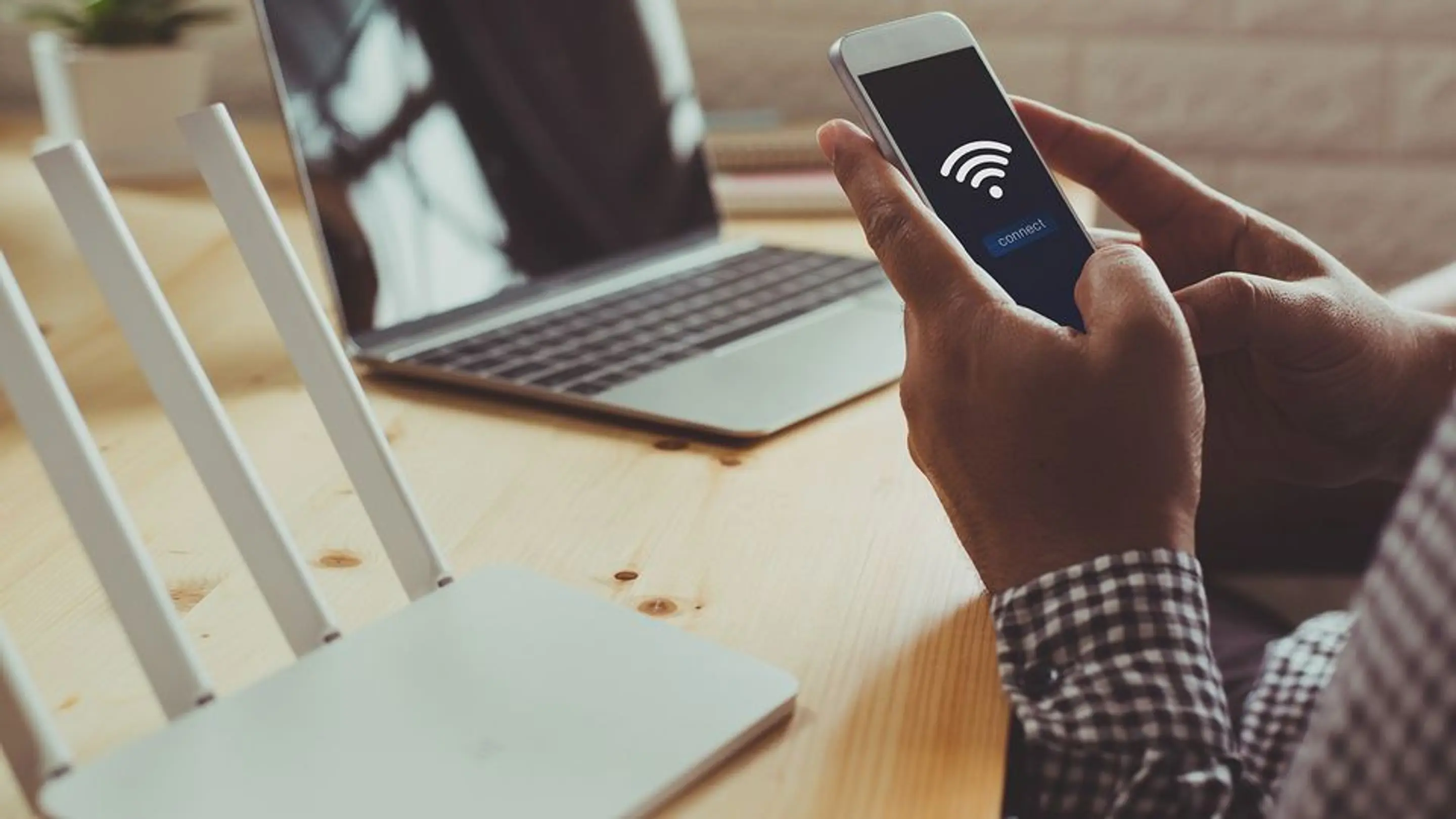Bilde av en person som setter opp et wifi-nettverk hjemme med pc i bakgrunnen og mobilen i hånda.