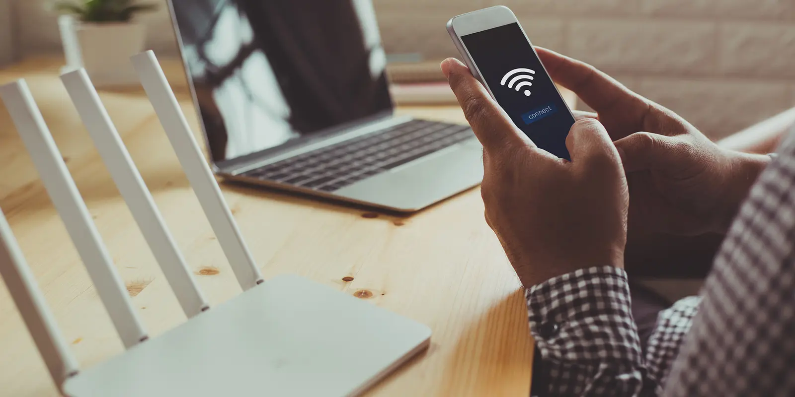 Bilde av en person som setter opp et wifi-nettverk hjemme med pc i bakgrunnen og mobilen i hånda.