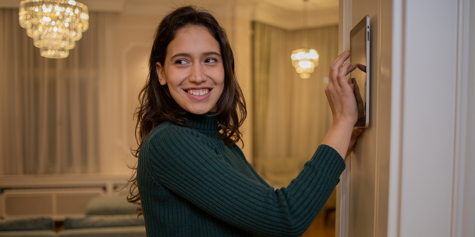 En person står i ett ljust hem och justerar en digital enhet monterad på väggen.