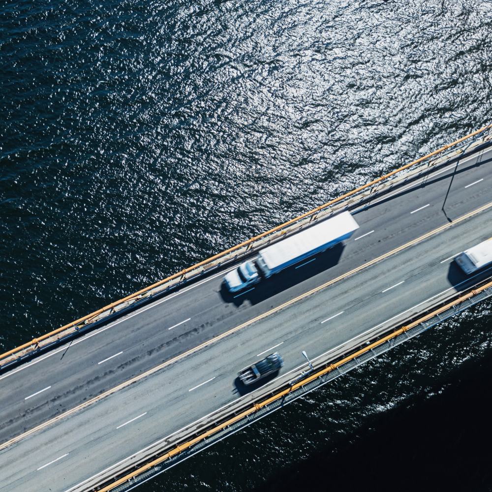 Flyttbil kör över stor bro över vatten. Transporterar bohag mellan länder.