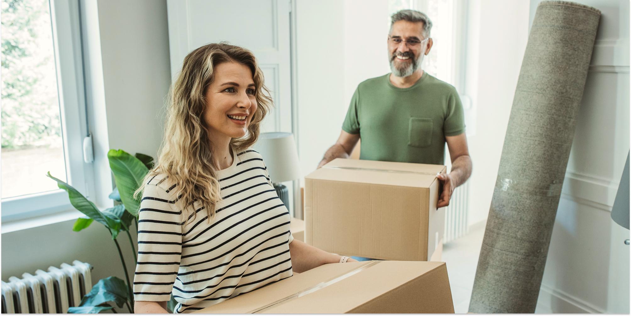 Ett par bär in kartonger i sin nya lägenhet och ser glada ut.
