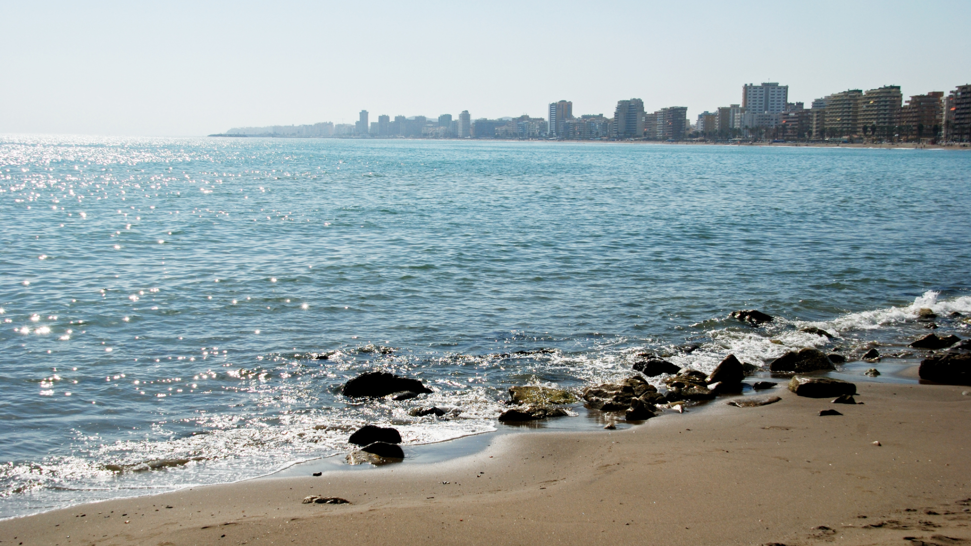 Sandstrand vid havet i Fuengirola. I bakgrunden syns en lång kustlinje med höga hus längs stranden.