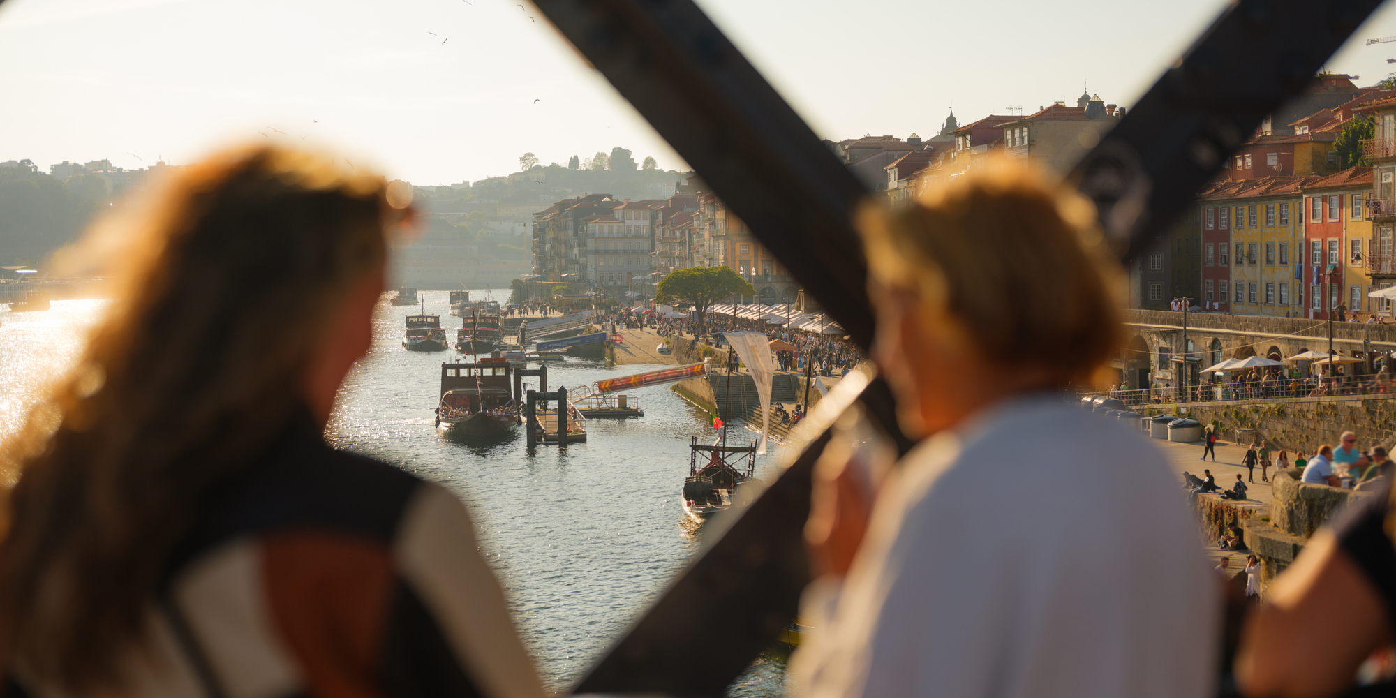 Två personer på en bro blickar ut över floden Douro i Porto, med båtar och färgglada hus i bakgrunden.