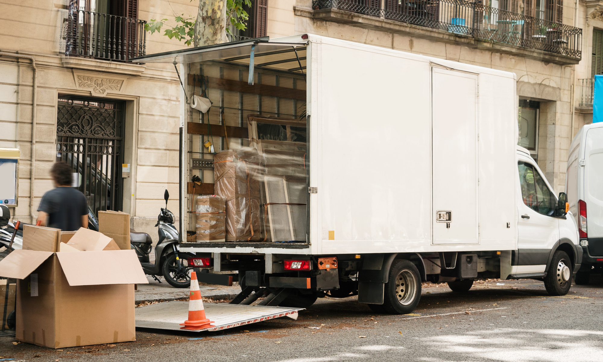 En flyttbil står parkerad utanför ett bostadshus medan flyttlådor och möbler lastas in.