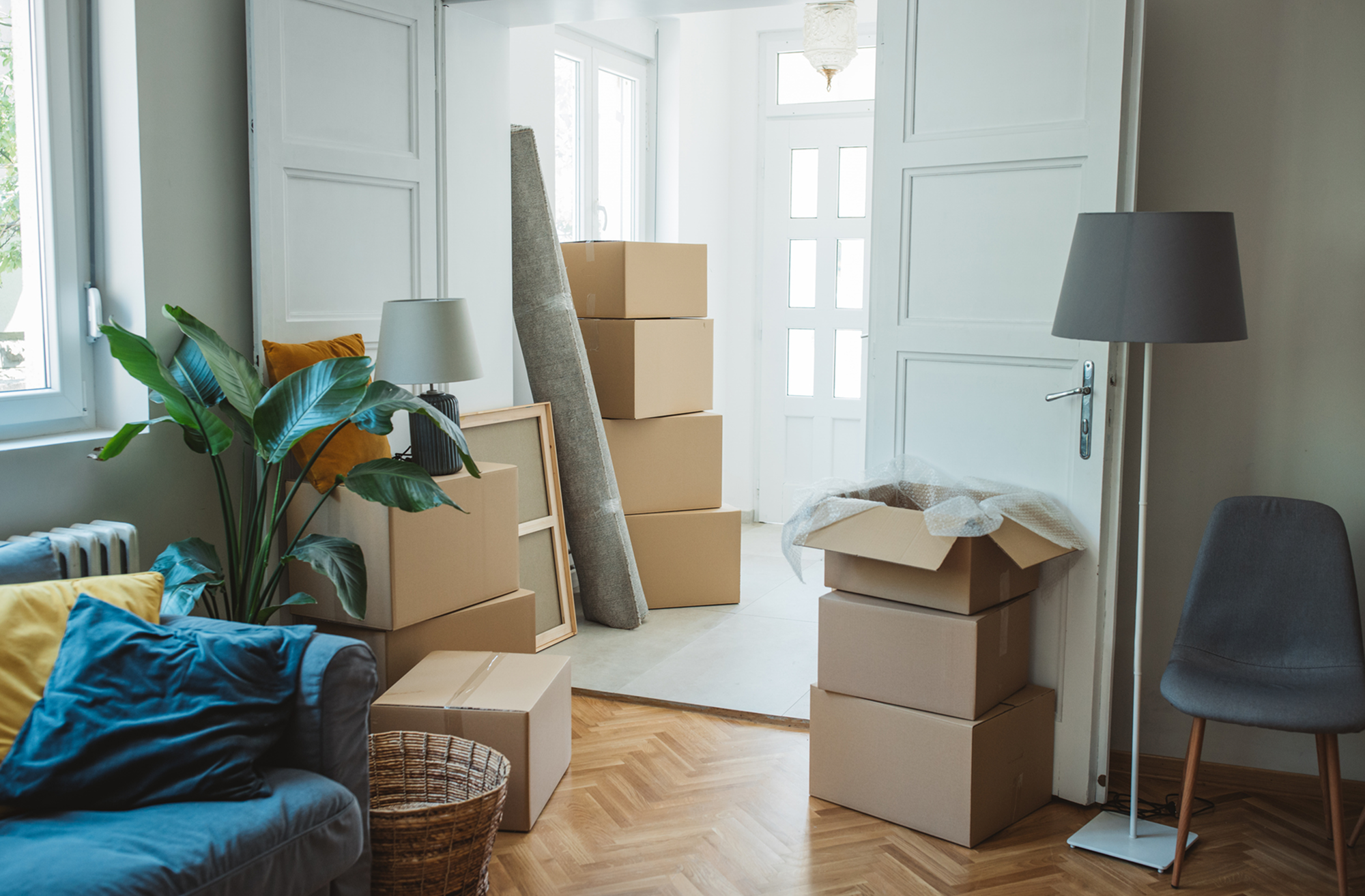 Flyttkartonger och möbler staplade i ett ljust vardagsrum.