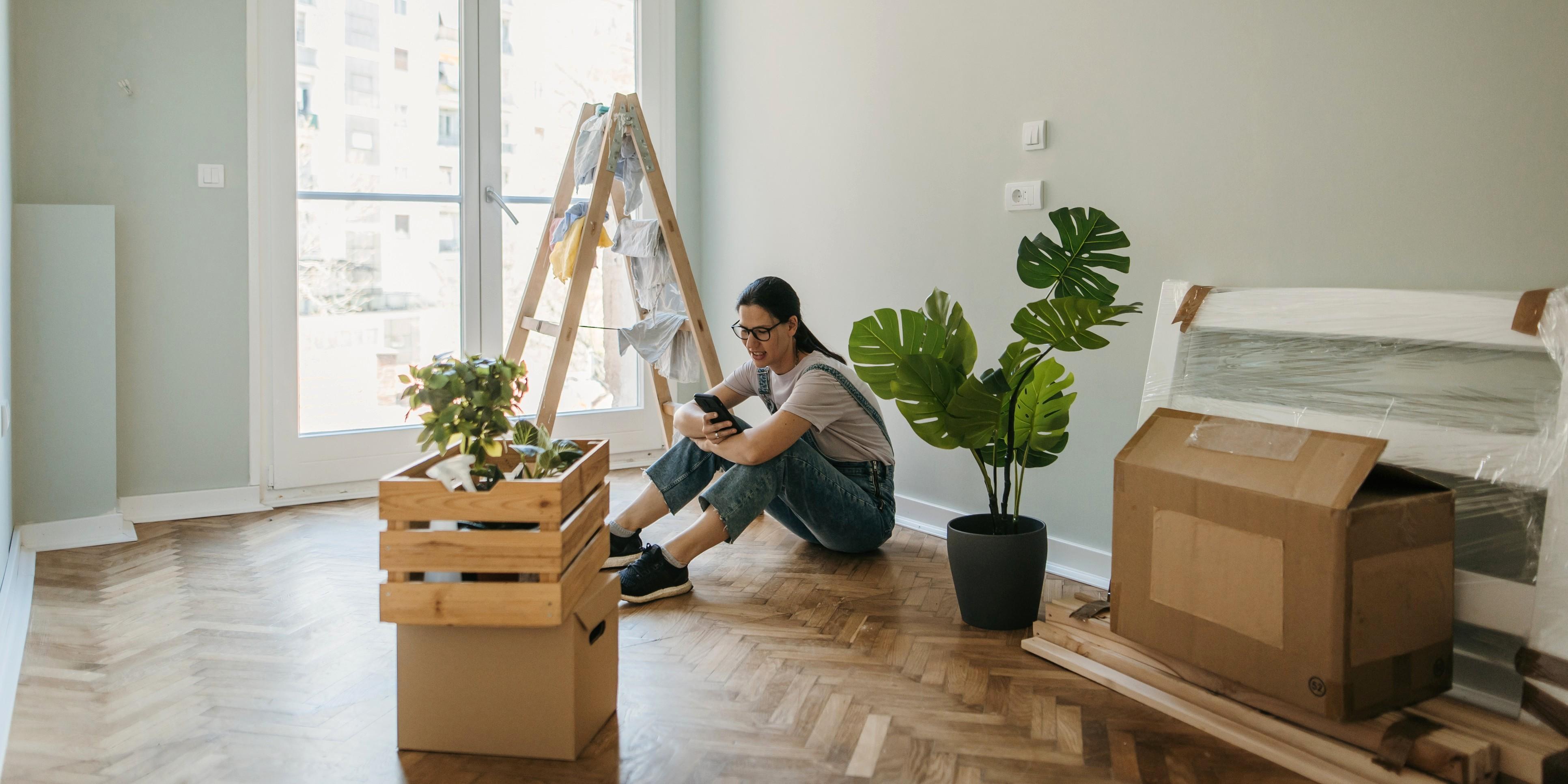 En kvinna i hängselbyxor sitter på golvet mitt bland alla sina saker hon packat ihop.