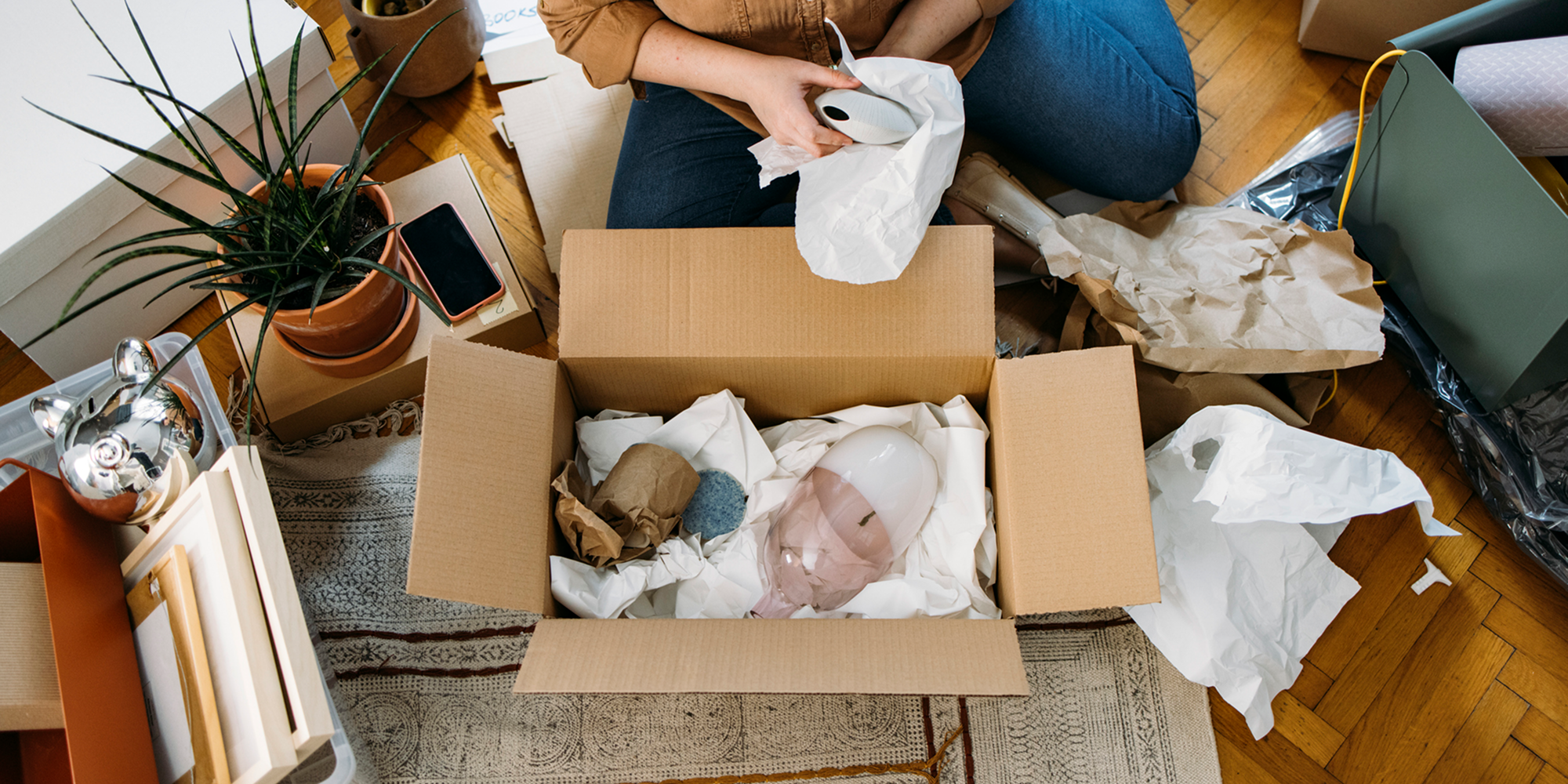 En person sitter på golvet och packar saker i en flyttkartong.