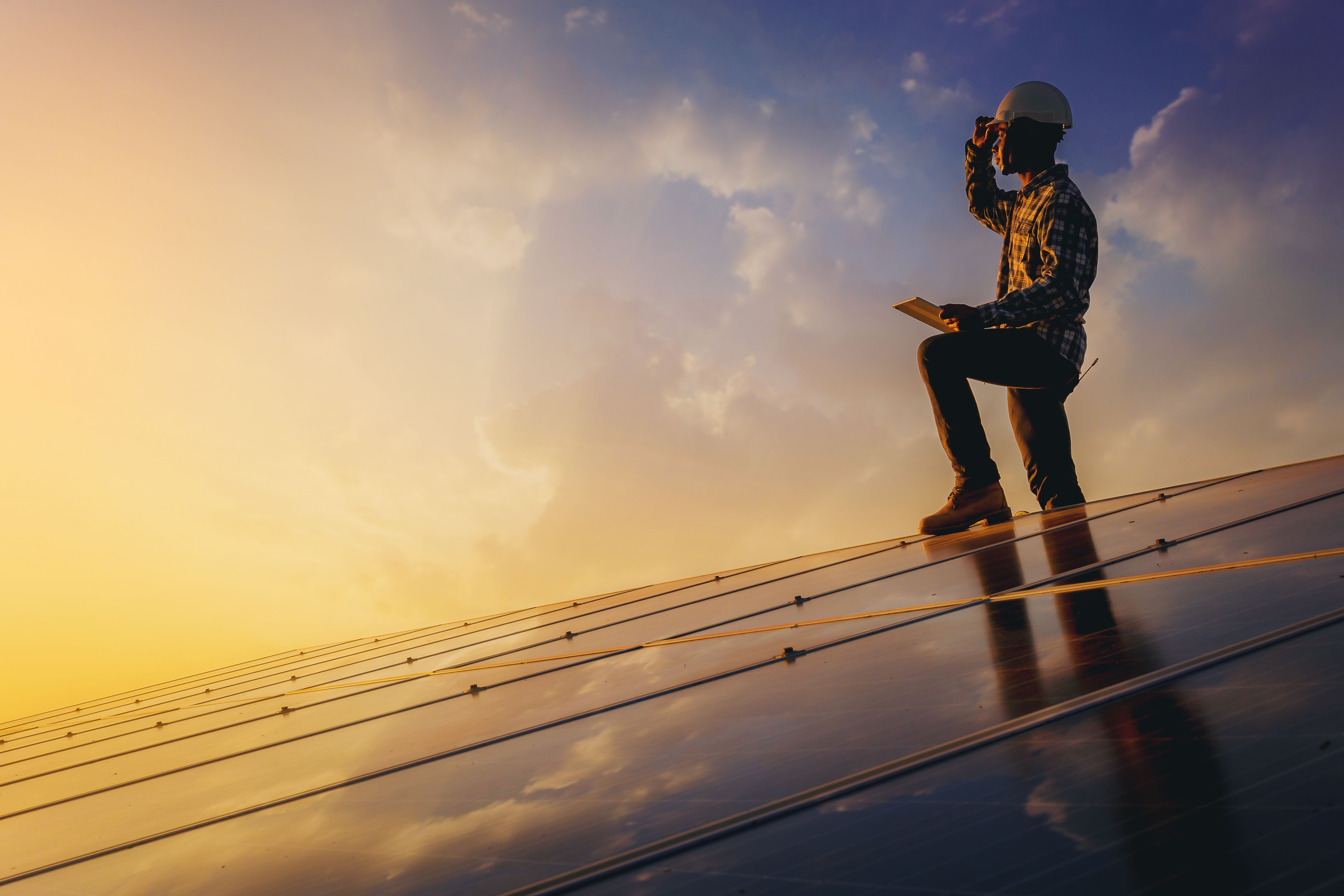 Tecnico che ispeziona dei pannelli solari al tramonto, energia fotovoltaica.