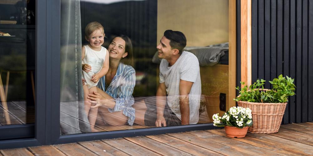 En mamma, pappa och tvååring tittar ut ur fönstret från sitt nybyggda hus.