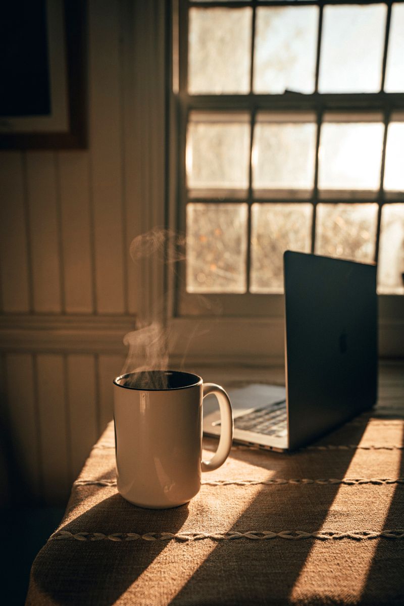 bilde av datamaskin og kaffekopp på et bord foran vindu