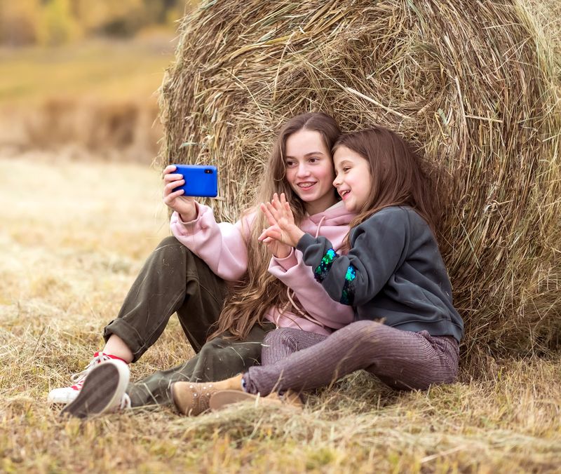 bilde-av-to-jenter-med-mobiltelefon-som-poserer-foran-en-høyball