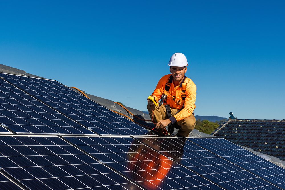 Un technicien installe des panneaux photovoltaïques sur un toit en souriant
