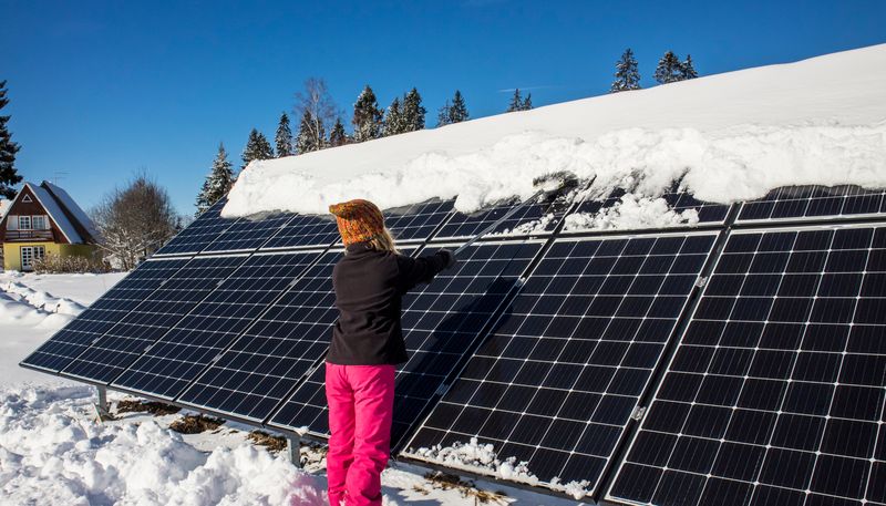 Kvinne fjerner snø fra solcellepanel på et tak