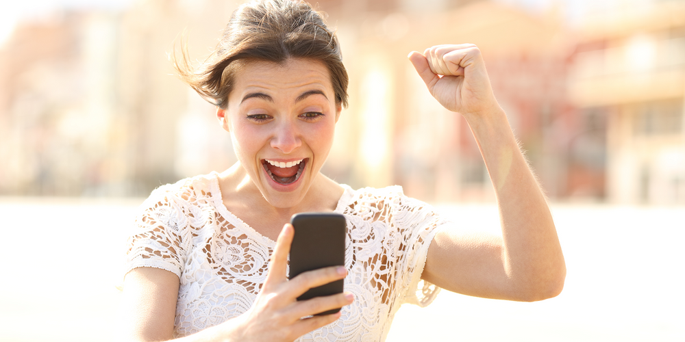 En kvinna har nyss vunnit en budgivning och tittar glatt på sin mobiltelefon.