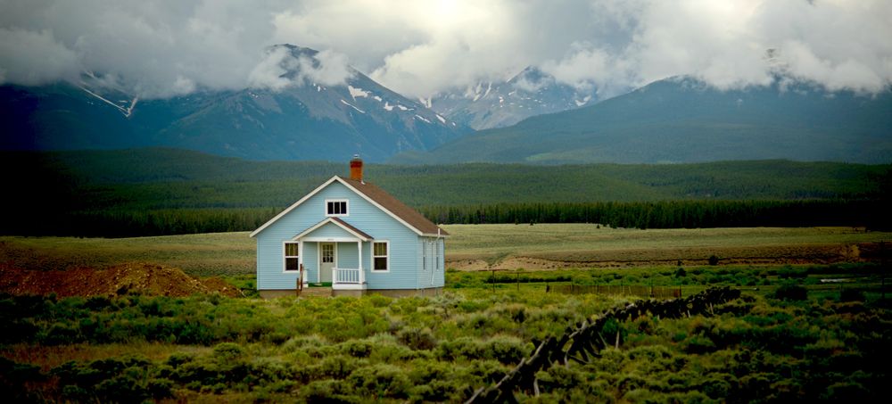 Ett blått hus med berg och skog i bakgrunden.